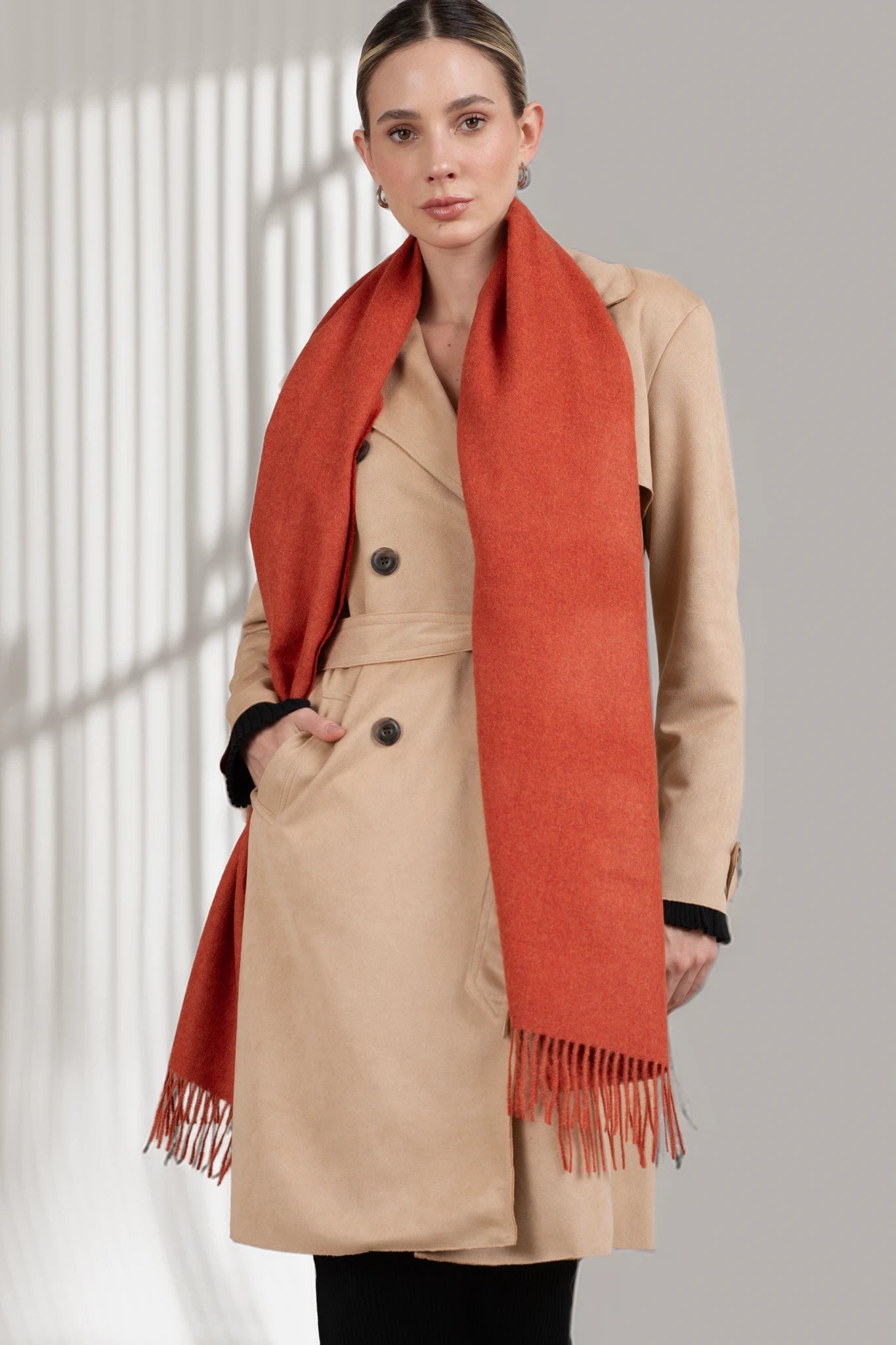 Woman wearing a beige coat and orange scarf against a neutral background