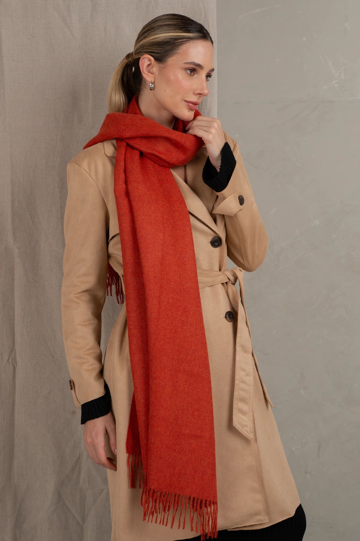 Woman wearing a beige coat and red scarf against a gray background