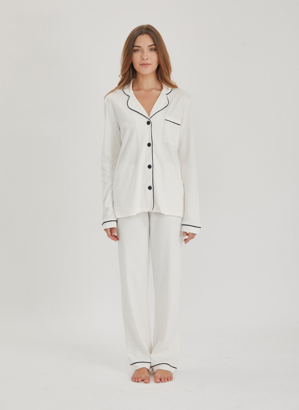 Woman wearing a white pima cotton pajama set with black piping on a light gray background