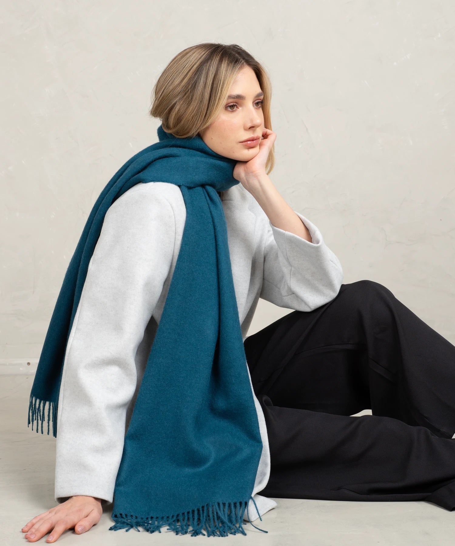 Woman wearing a teal scarf sitting on the floor against a plain background