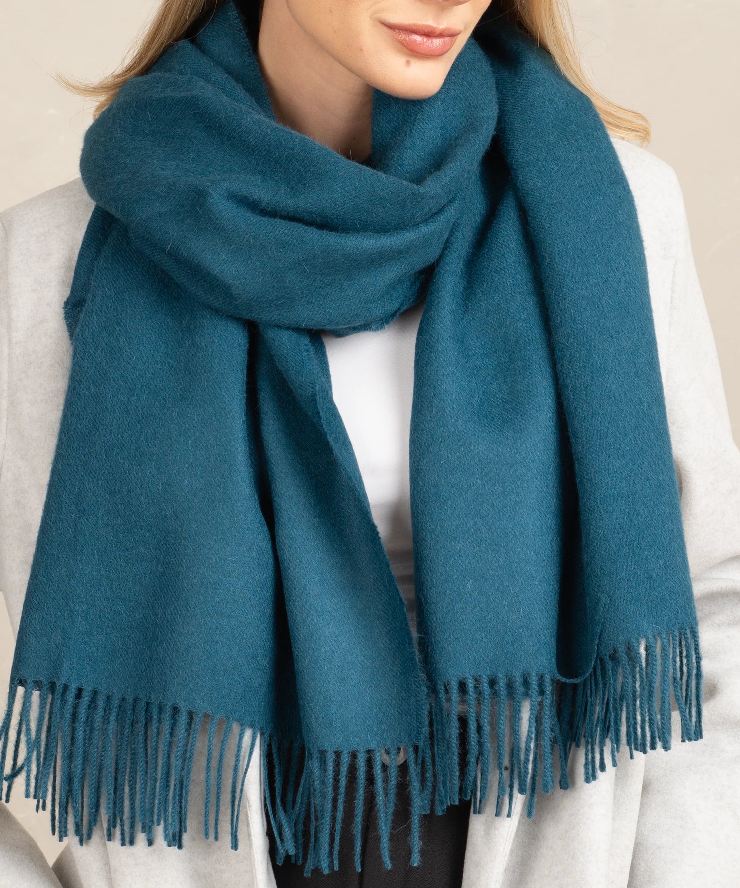 Teal scarf with fringe worn by a person on a neutral background