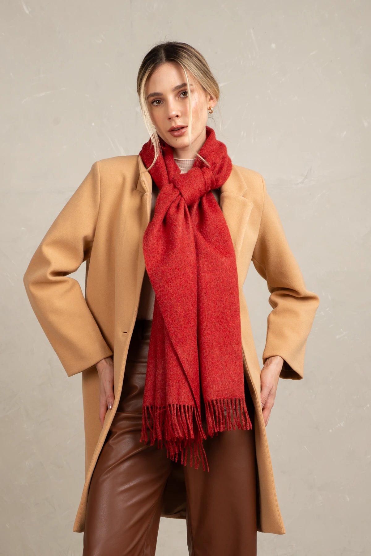 Woman wearing a tan coat and a inka fabric baby alpaca red scarf against a neutral background