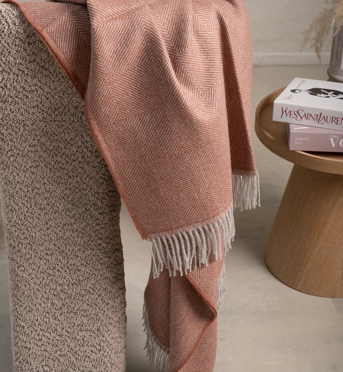 Pink woven blanket draped over a textured surface with a small wooden table in the background.