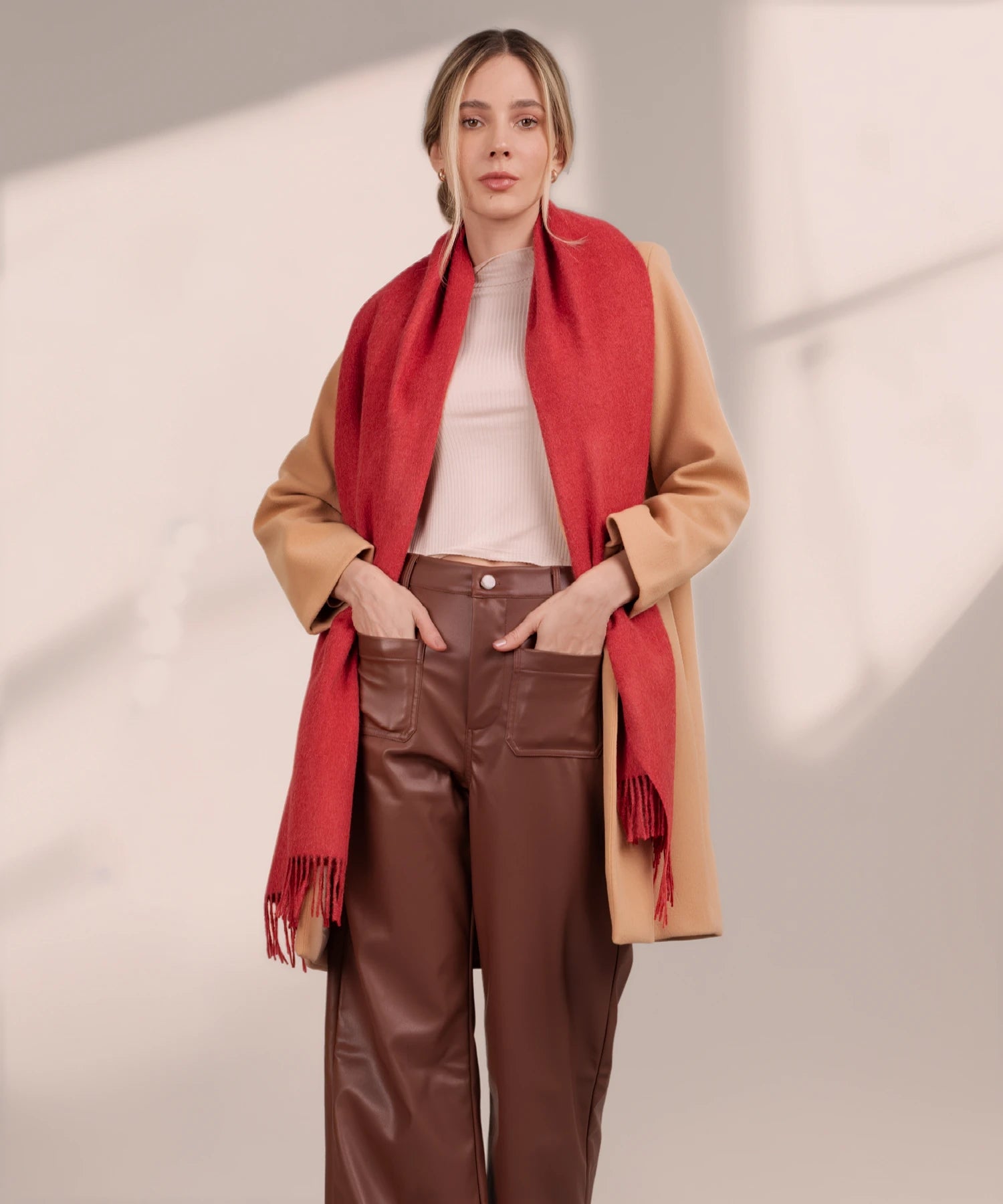 Woman wearing a beige coat, red scarf, and brown pants on a neutral background