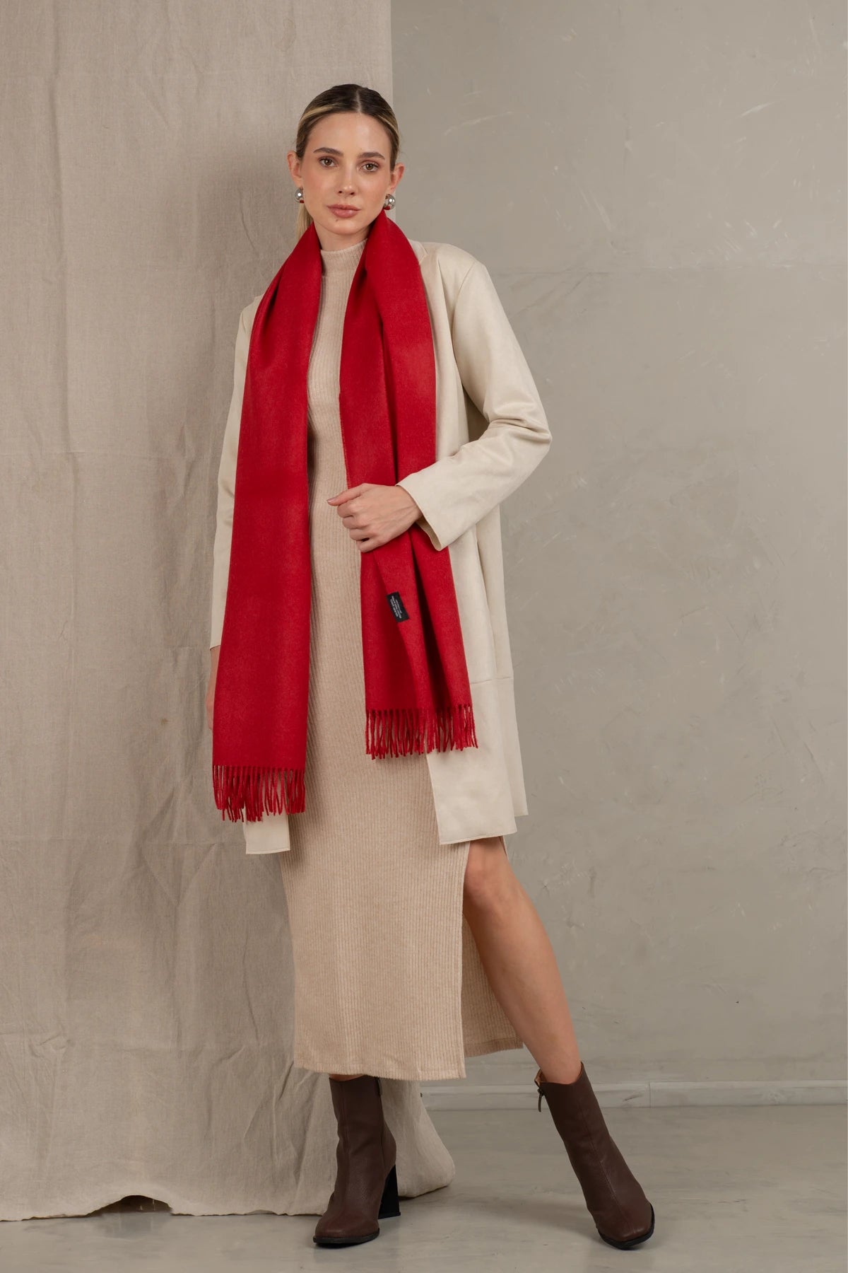 Woman wearing a 100% baby alpaca red scarf, beige coat, and dress against a plain background