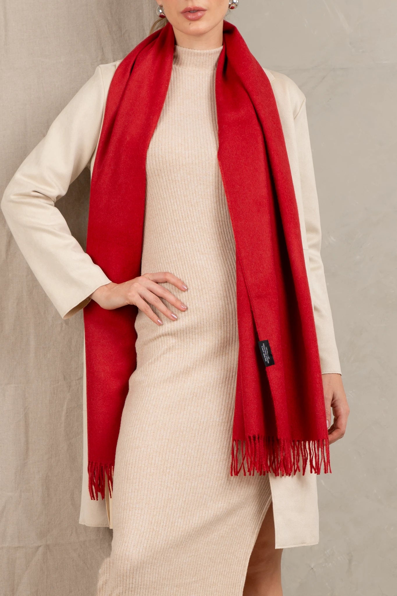 Person wearing a red peruvian alpaca  scarf and beige outfit against a neutral background