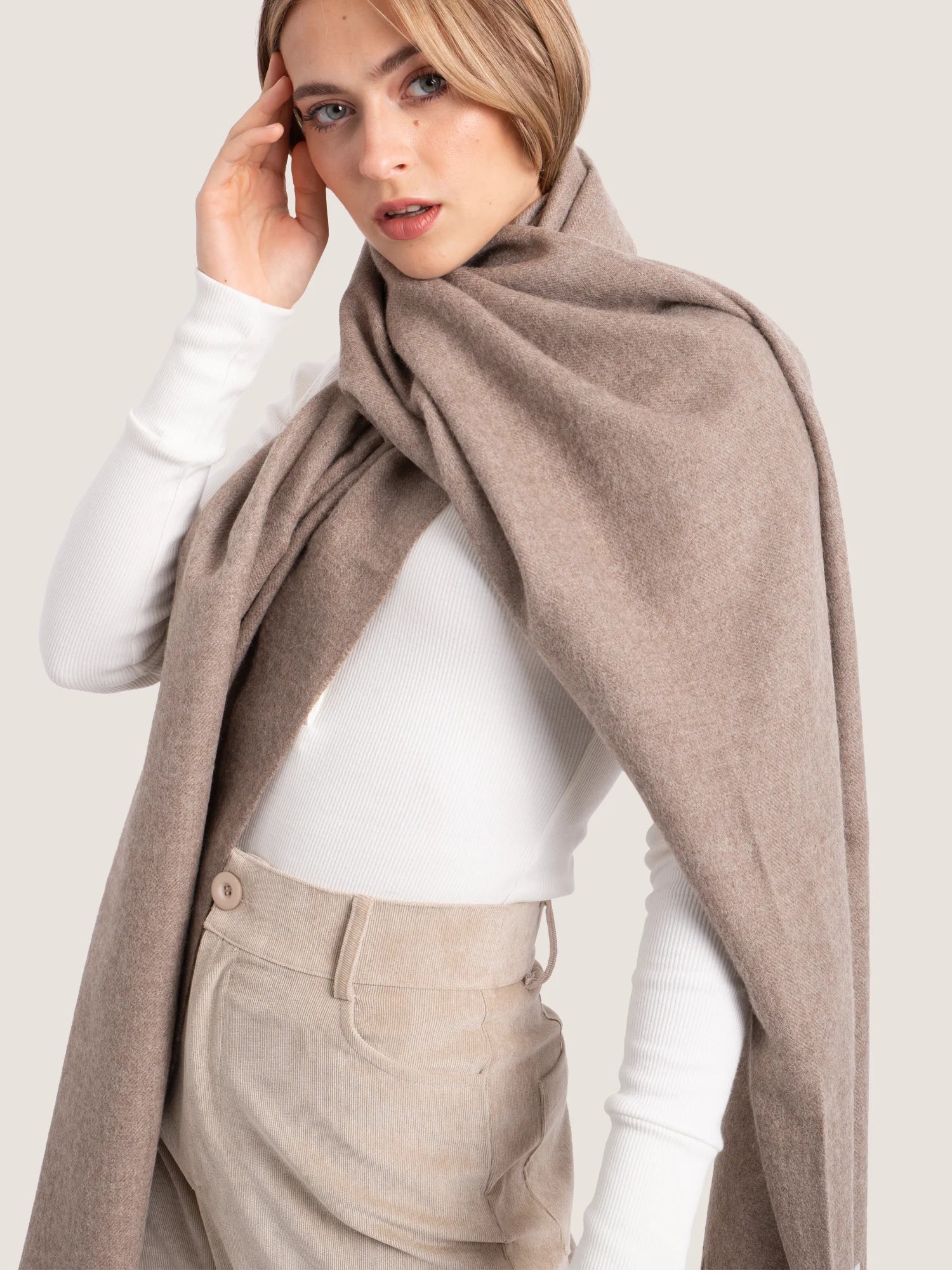 Woman wearing a beige scarf and pants on a plain background