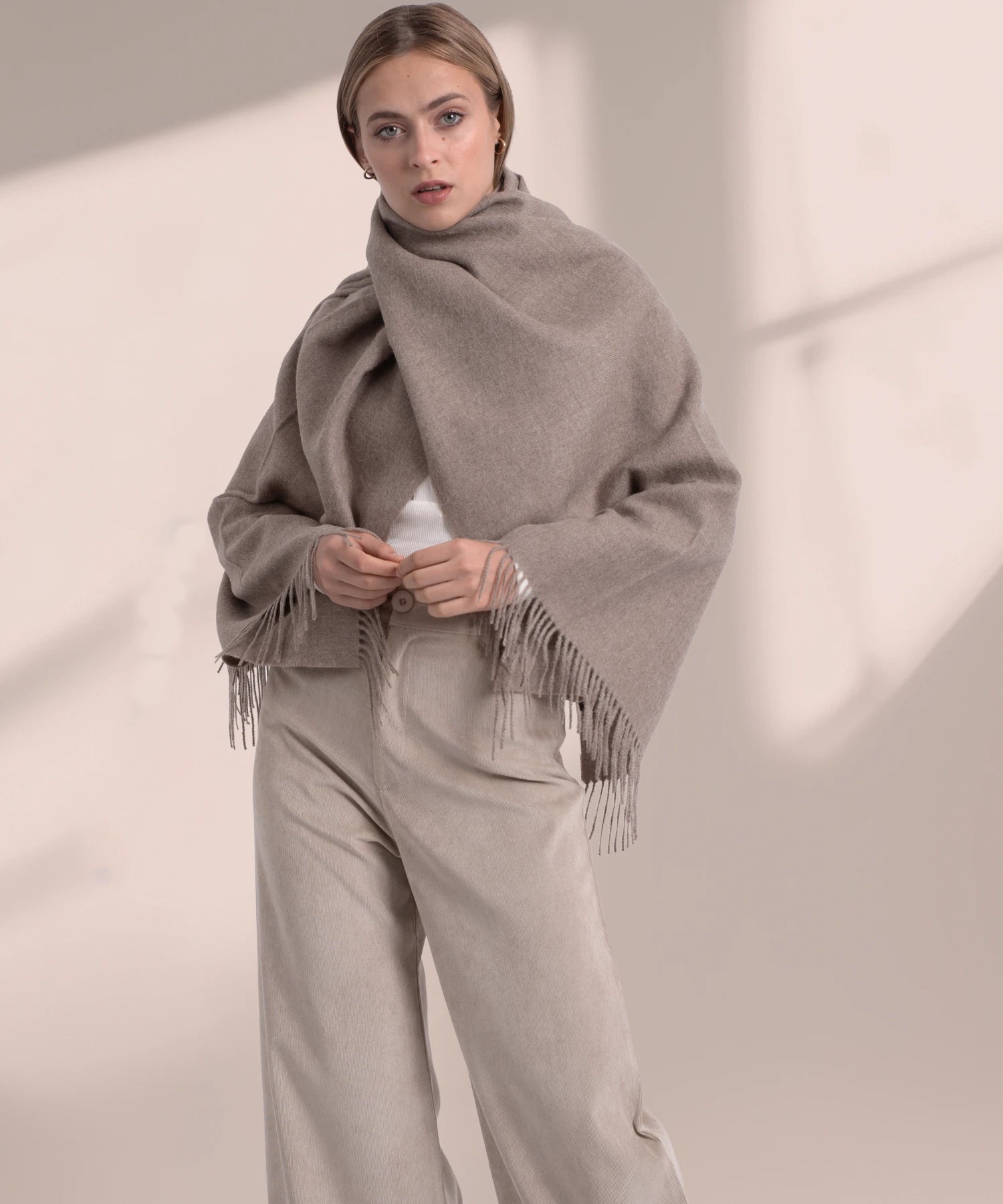 Woman wearing a beige scarf and pants against a neutral background