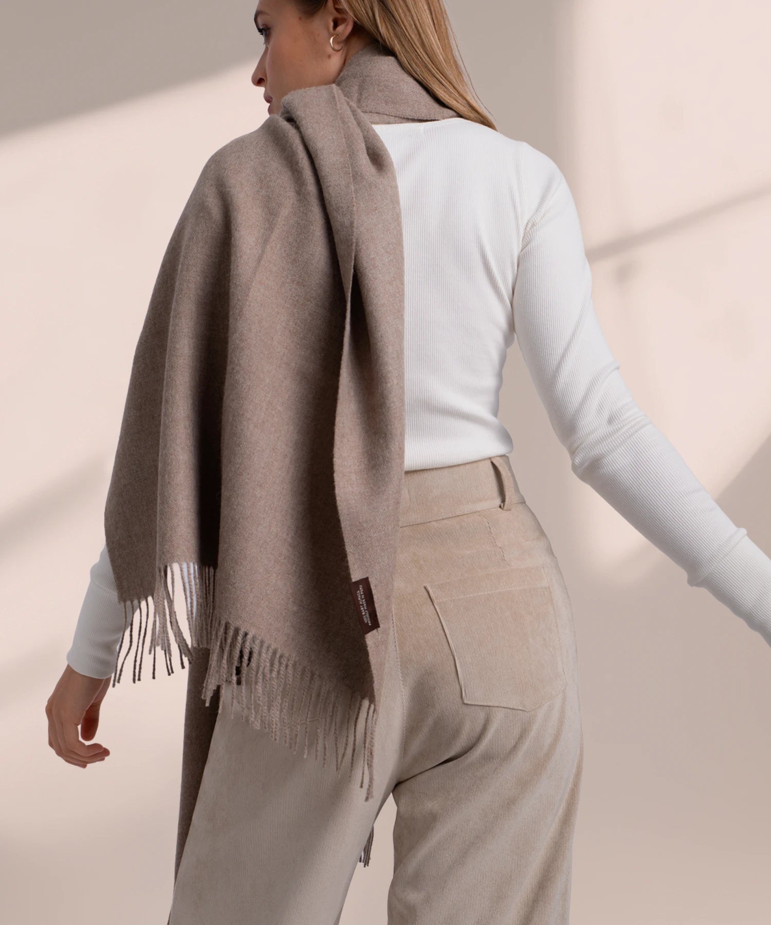 Woman wearing a brown scarf and beige pants against a neutral background