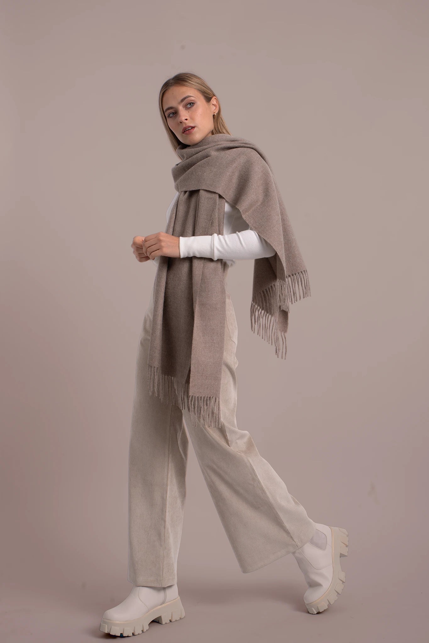 Woman wearing a large beige scarf with a plain background