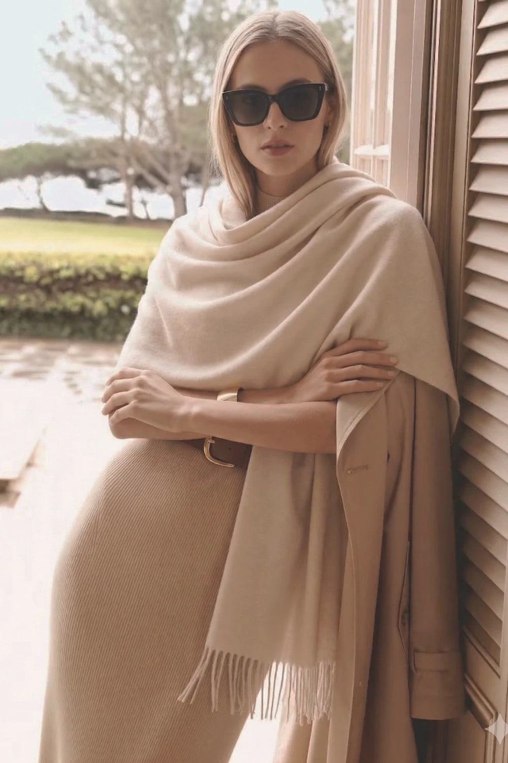 Woman wearing a beige scarf and sunglasses by a window with a scenic background