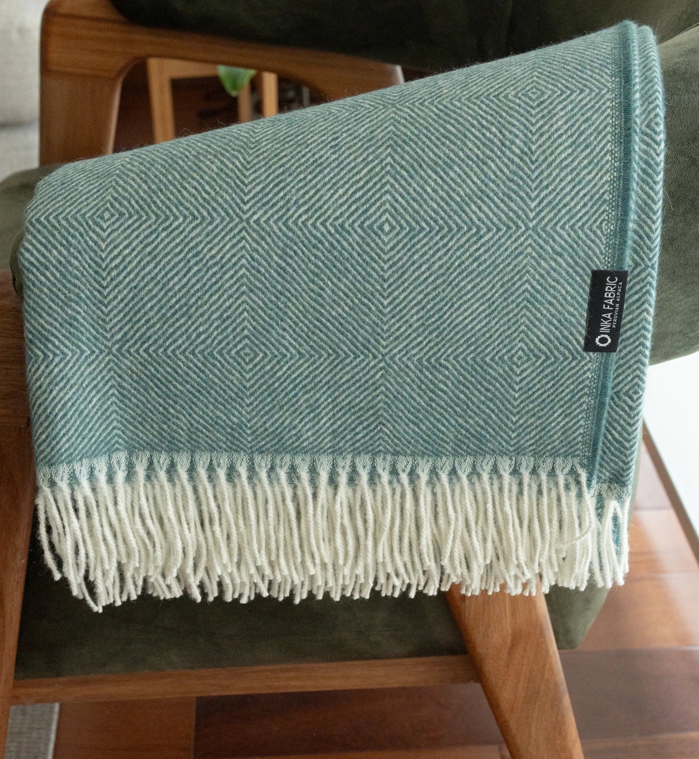 Teal patterned throw blanket with white fringe on a chair