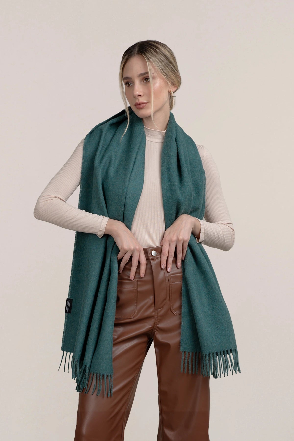 Woman wearing a baby alpaca  teal scarf, beige top, and brown pants on a beige background