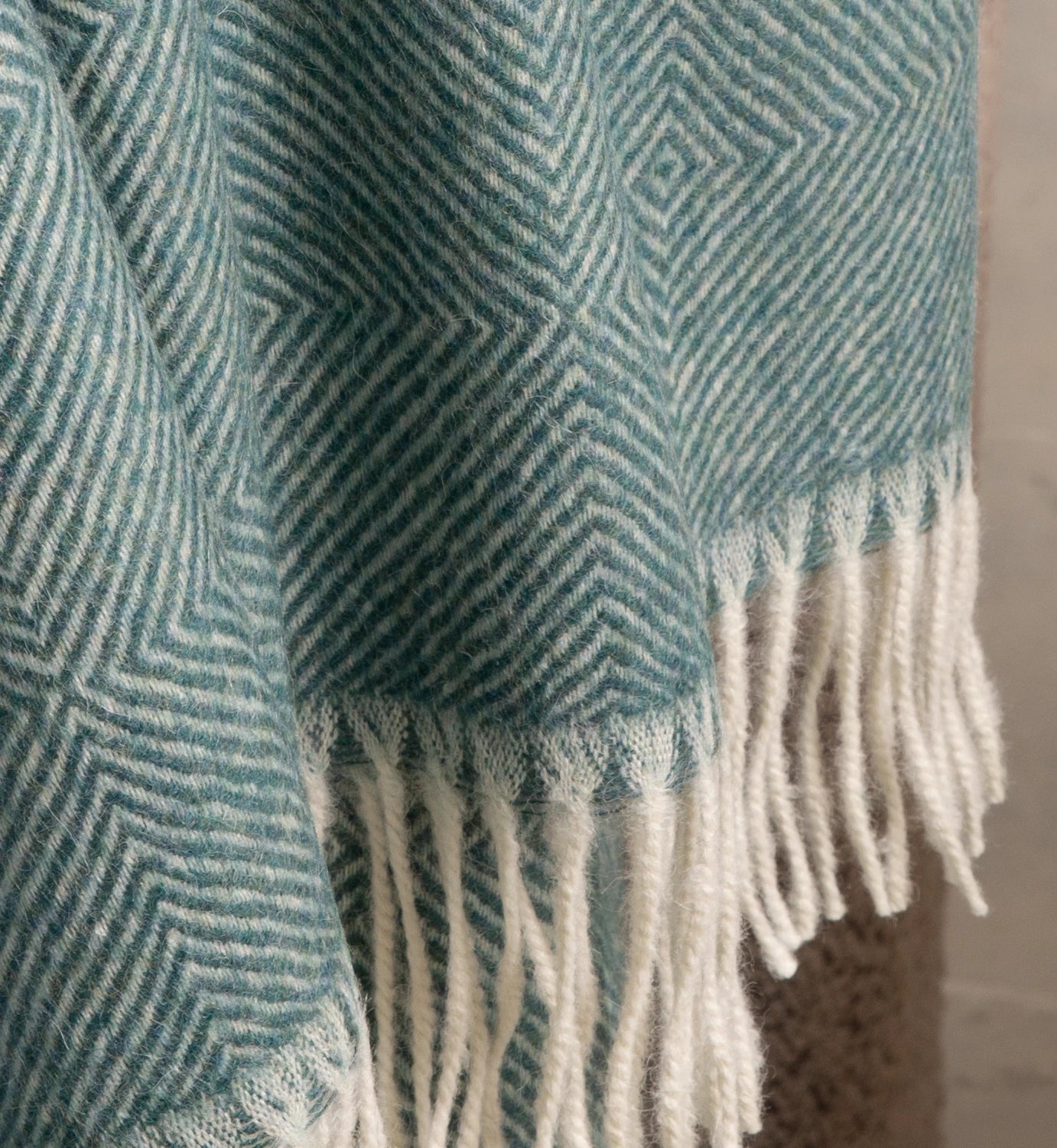 Teal and white patterned blanket with fringes on a neutral background