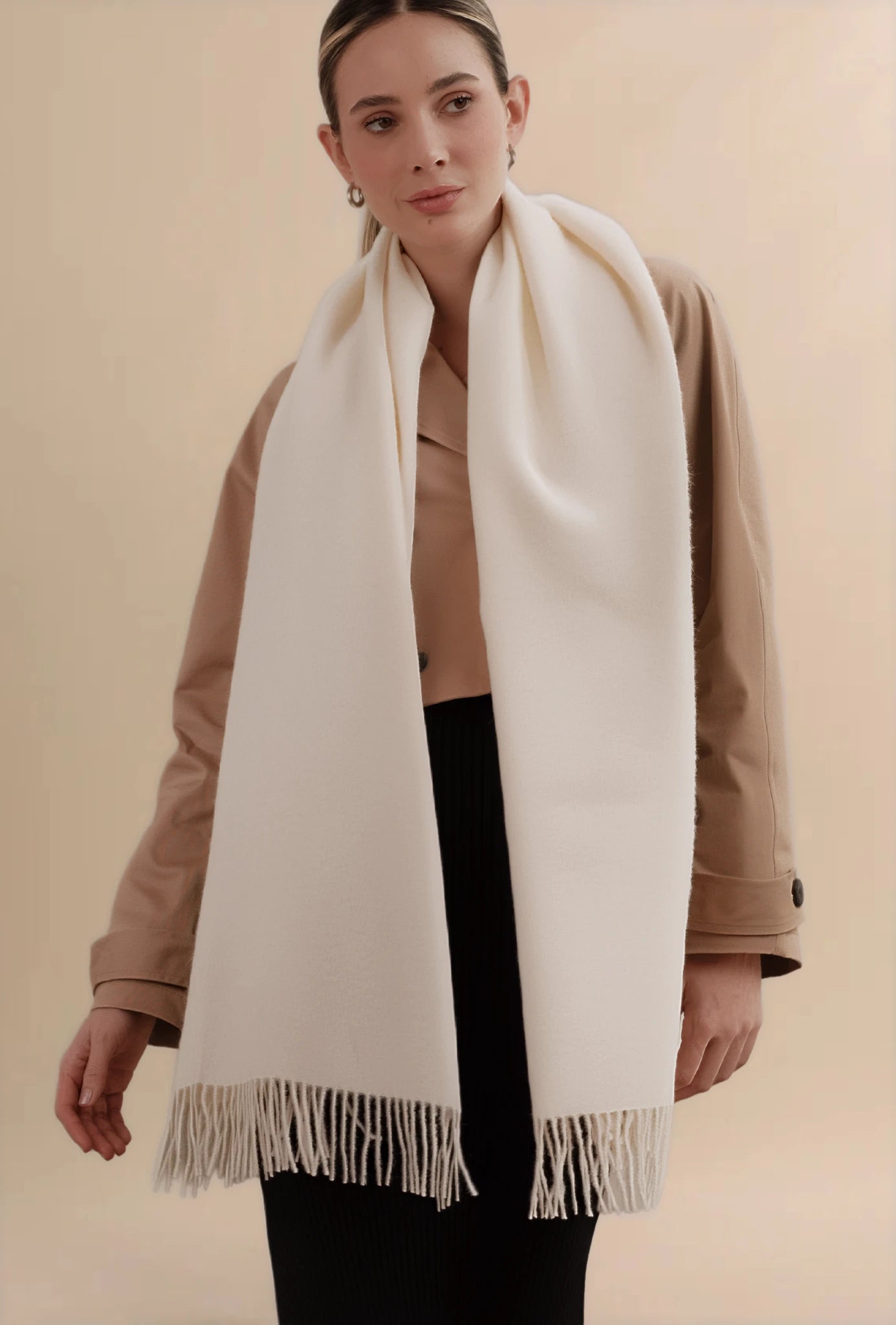 Woman wearing a beige scarf with fringe on a beige background