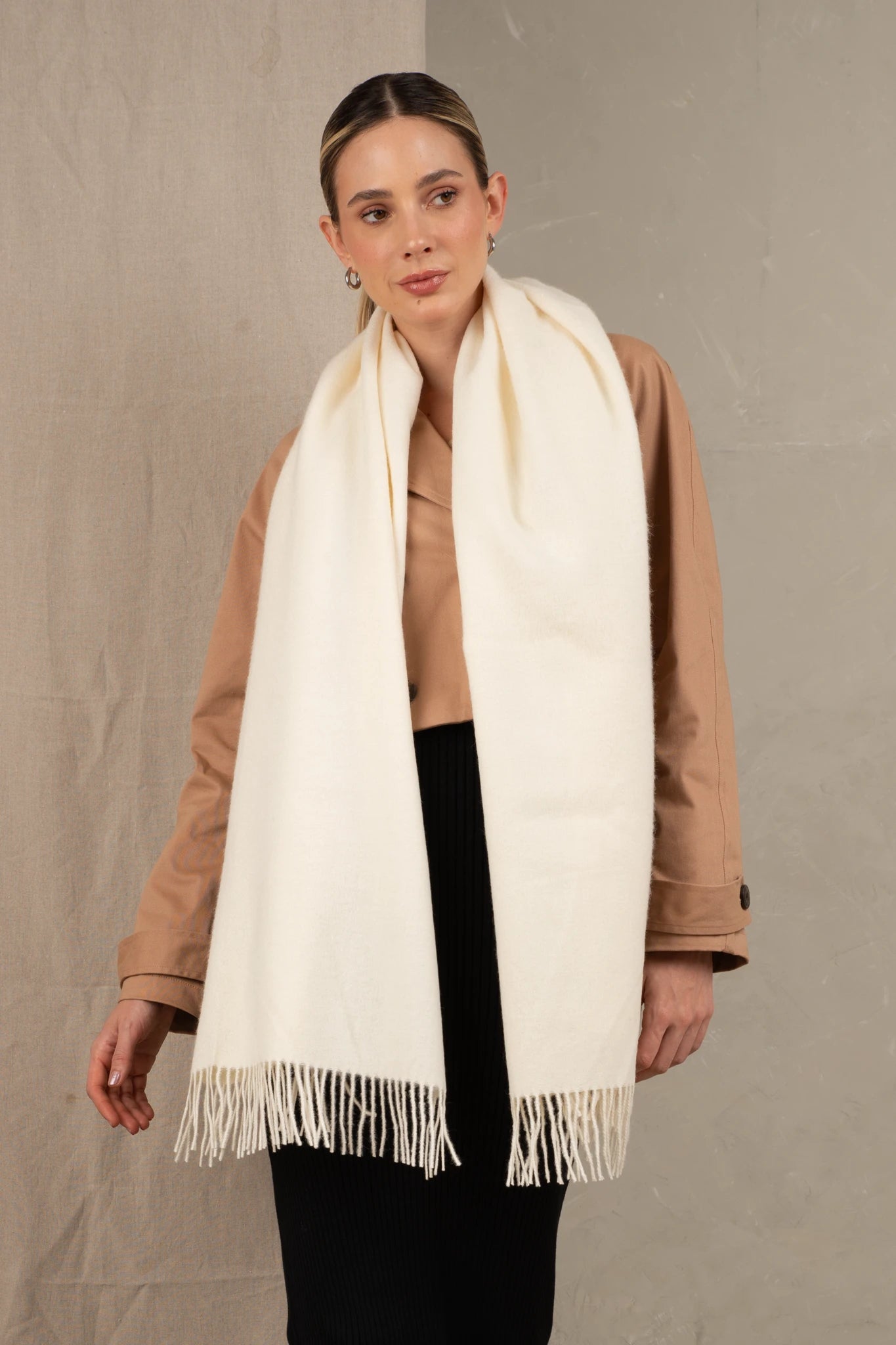 Woman wearing a beige scarf with fringe on a plain background