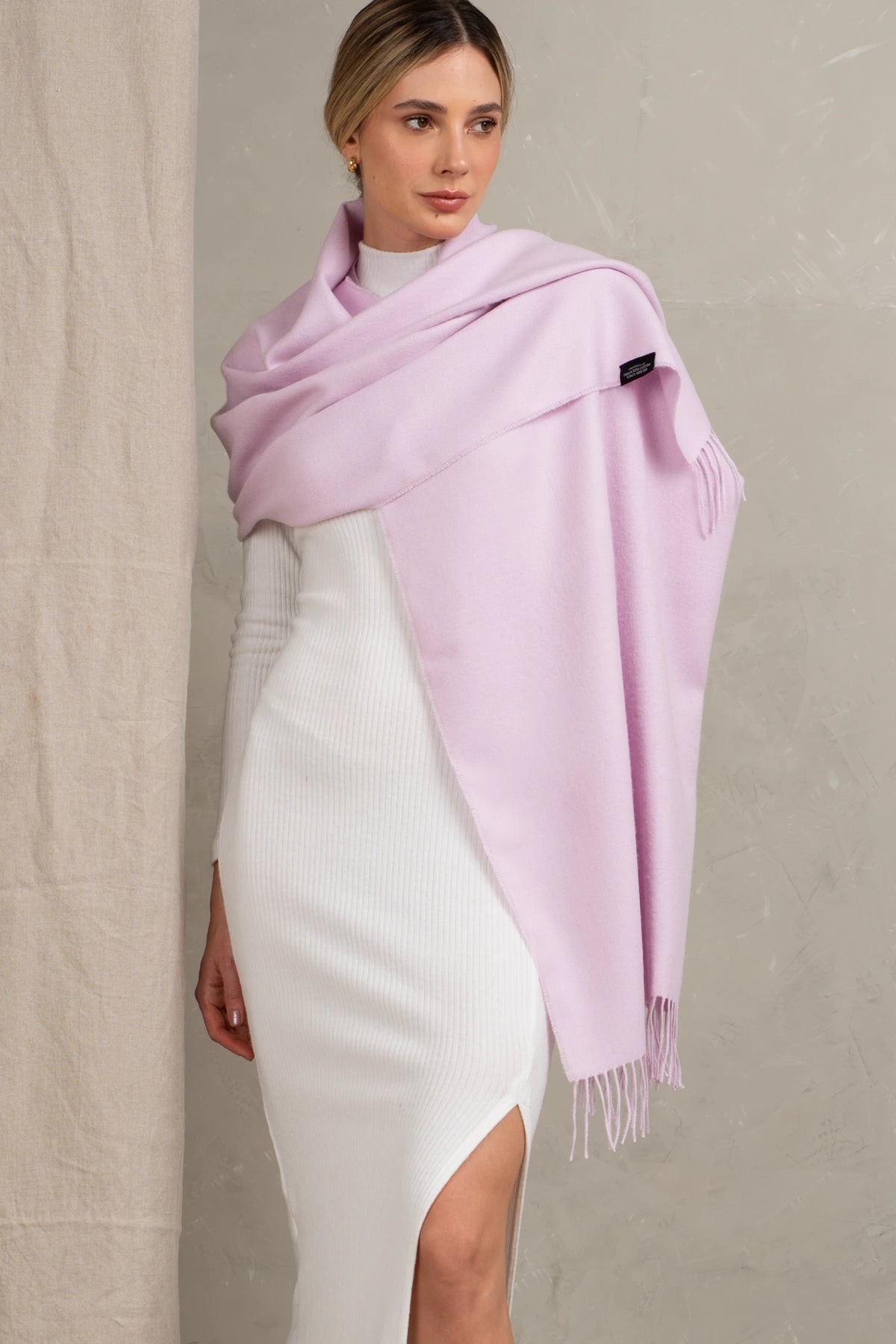 Woman wearing a baby alpaca light pink scarf with a brand logo against a neutral background