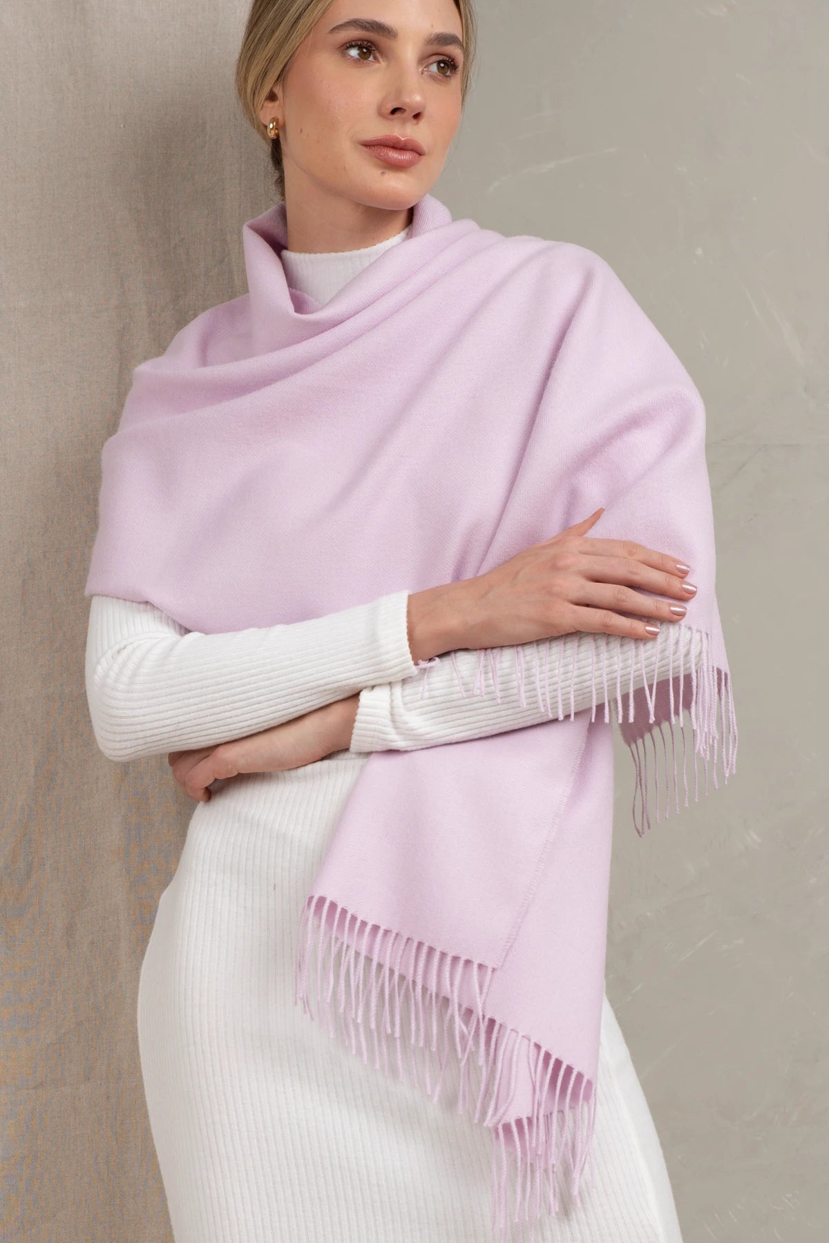 Woman wearing a light purple scarf with fringe on a plain background