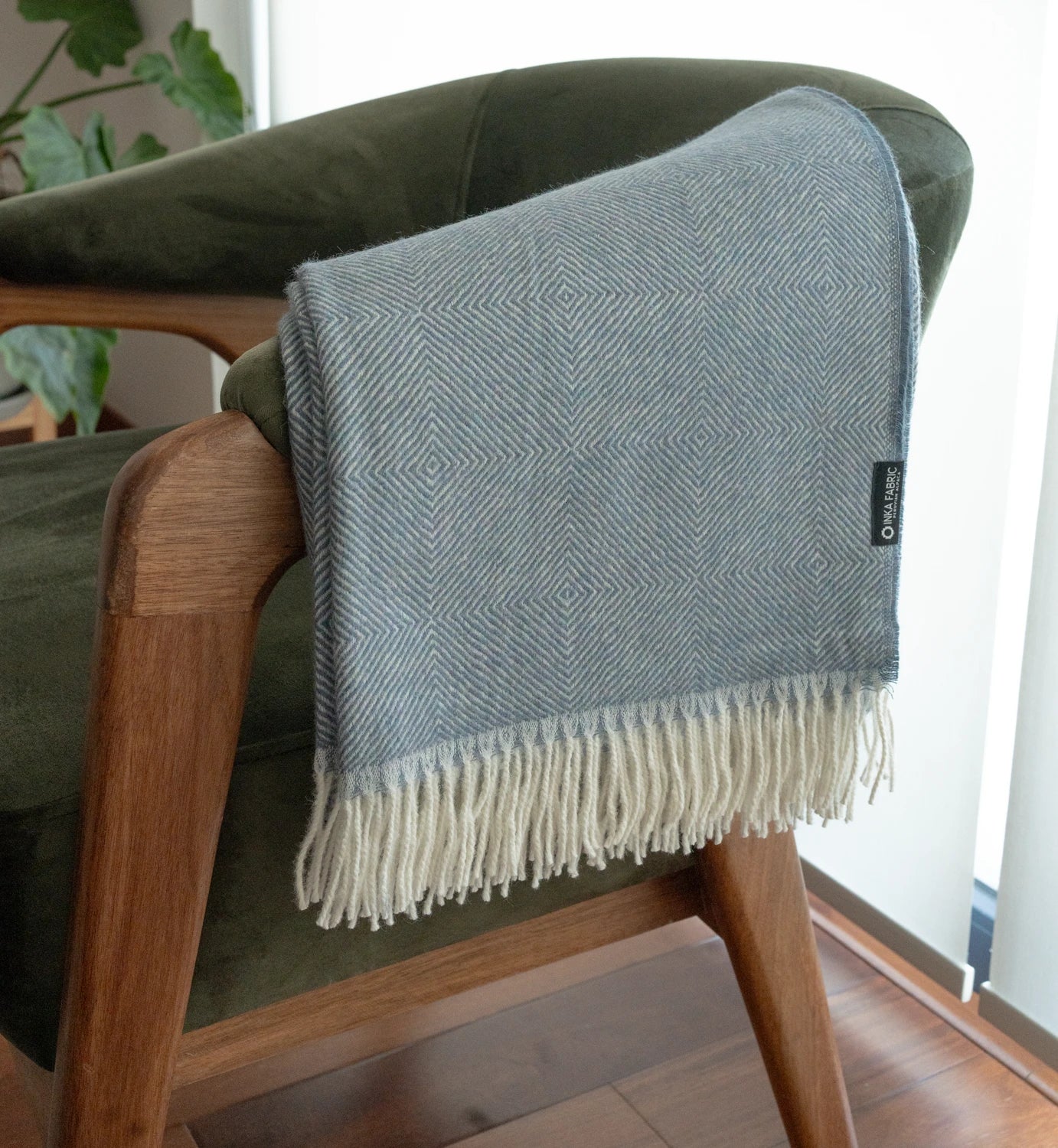 Gray woven throw blanket with fringes draped over a green chair.