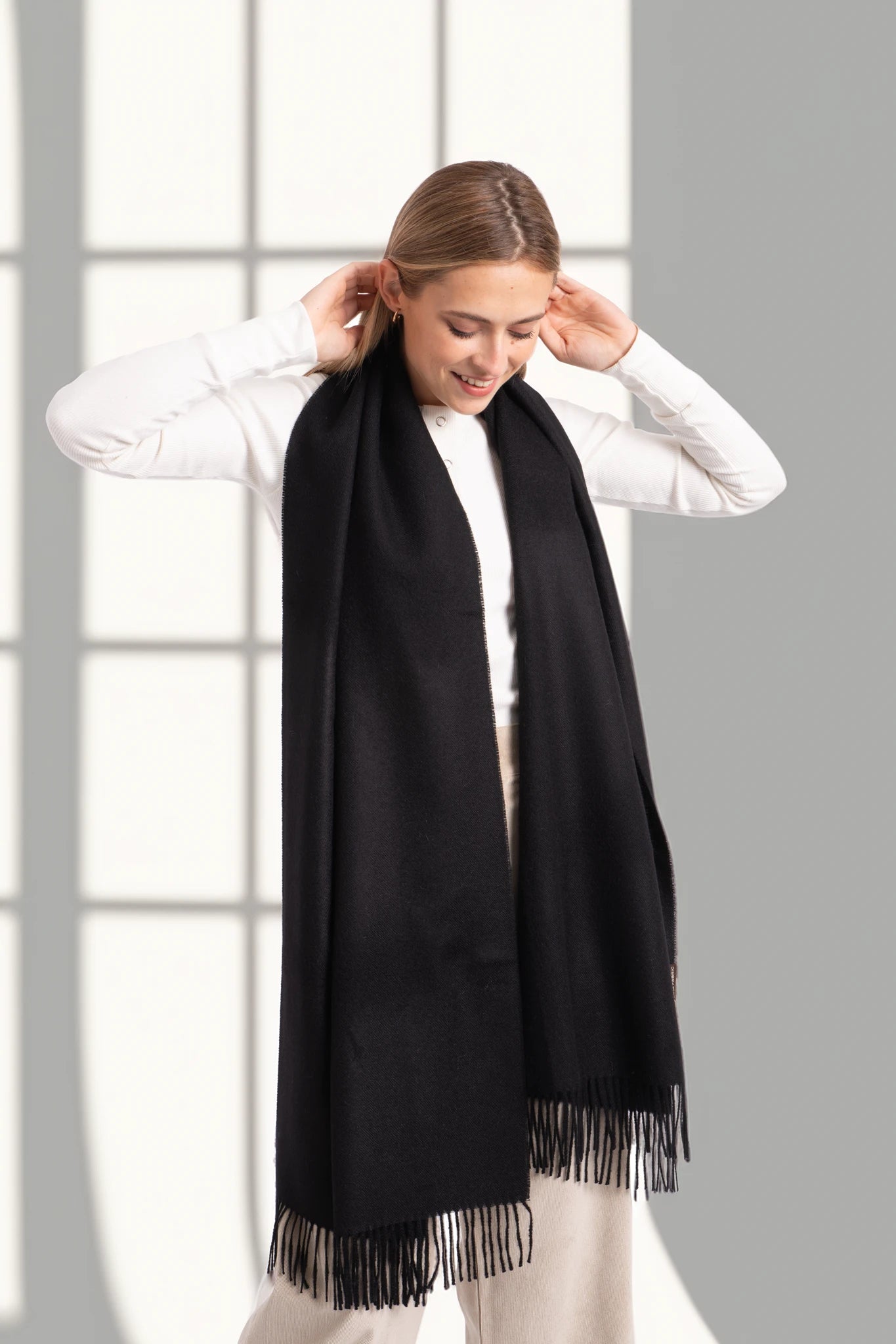 Person wearing a black scarf with fringe, standing against a light gray background