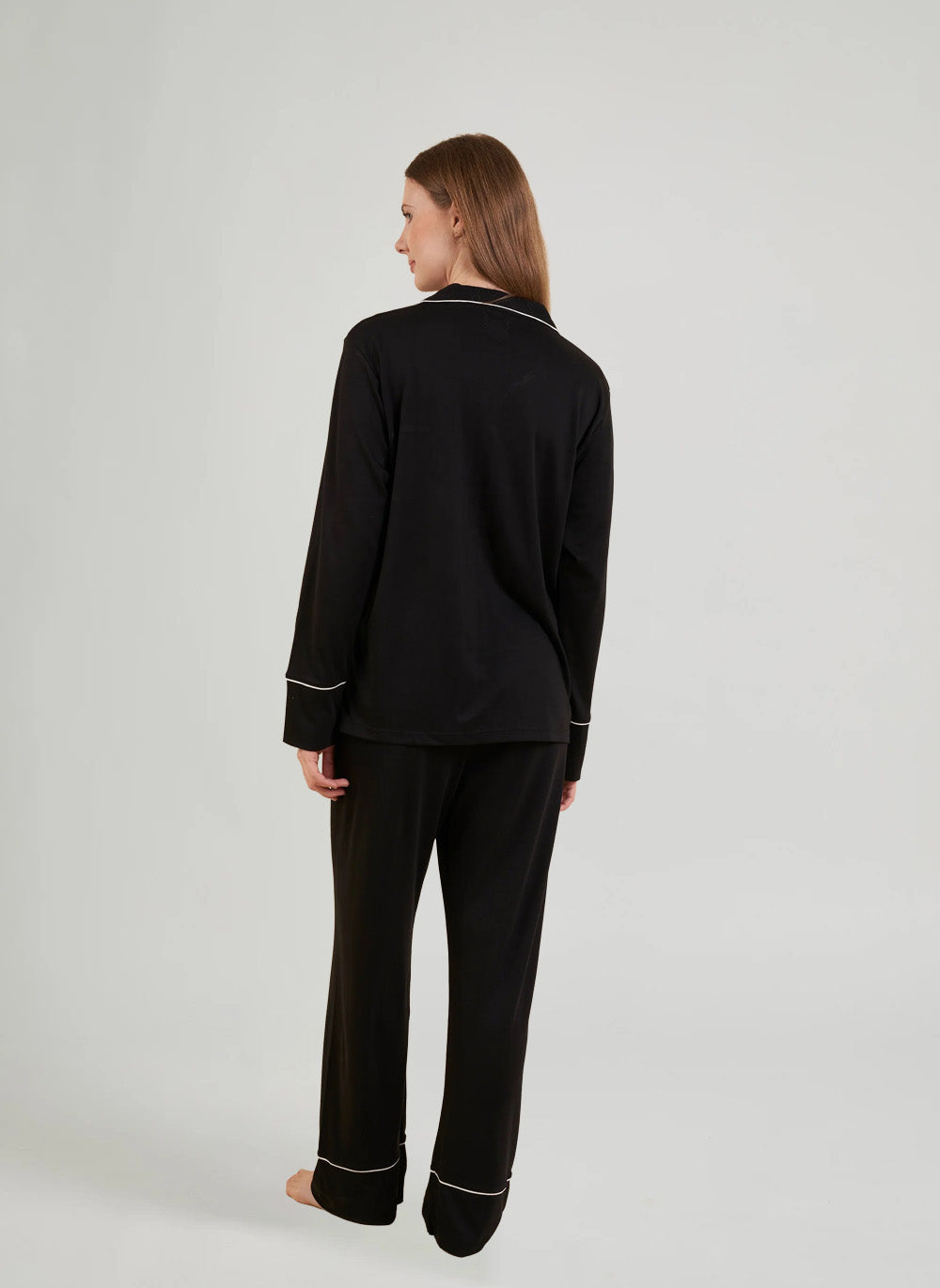 Woman wearing black pajamas with white piping on a light gray background
