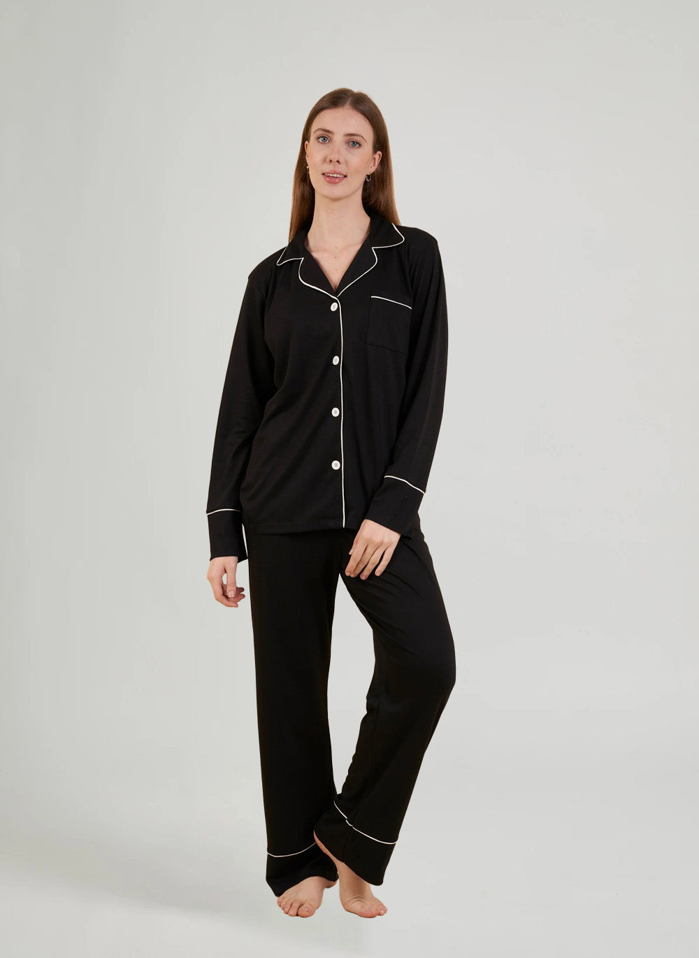 Woman wearing black pajamas with white piping on a gray background