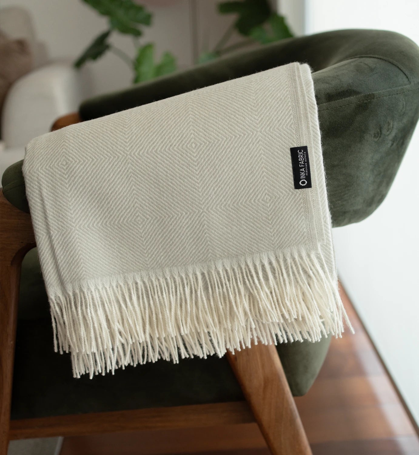 White textured throw blanket with fringe on a chair, featuring a brand label.