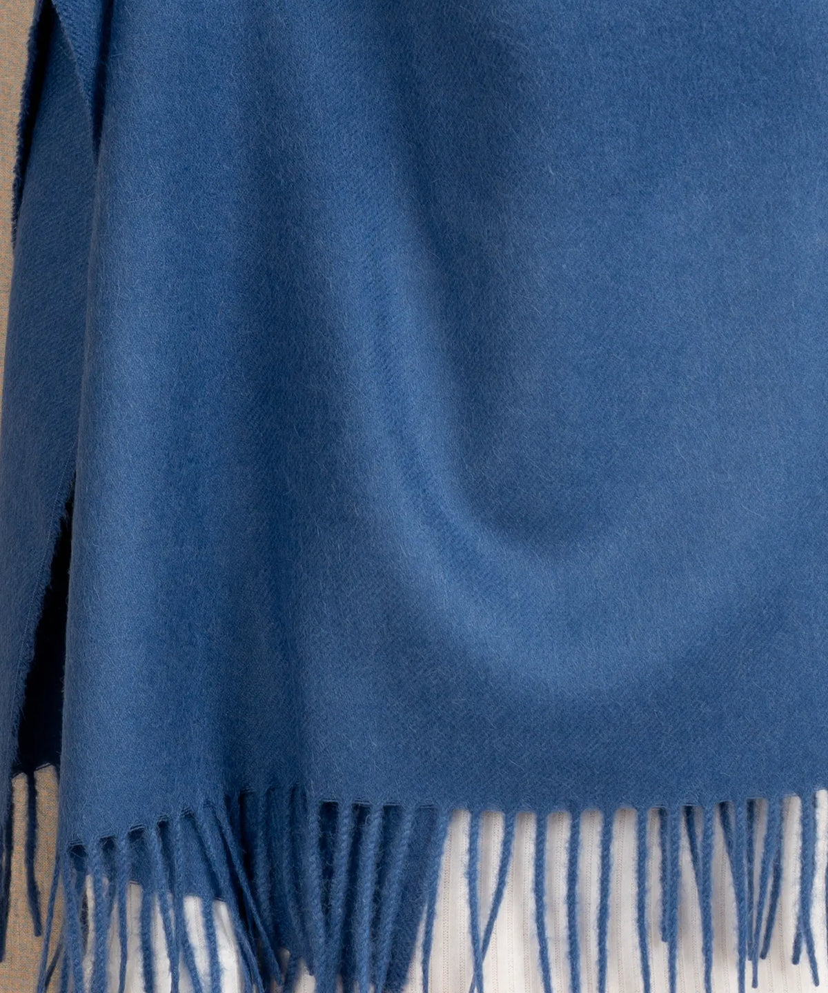 A close-up of a blue woven scarf with fringed edges, draped to show its texture and color.