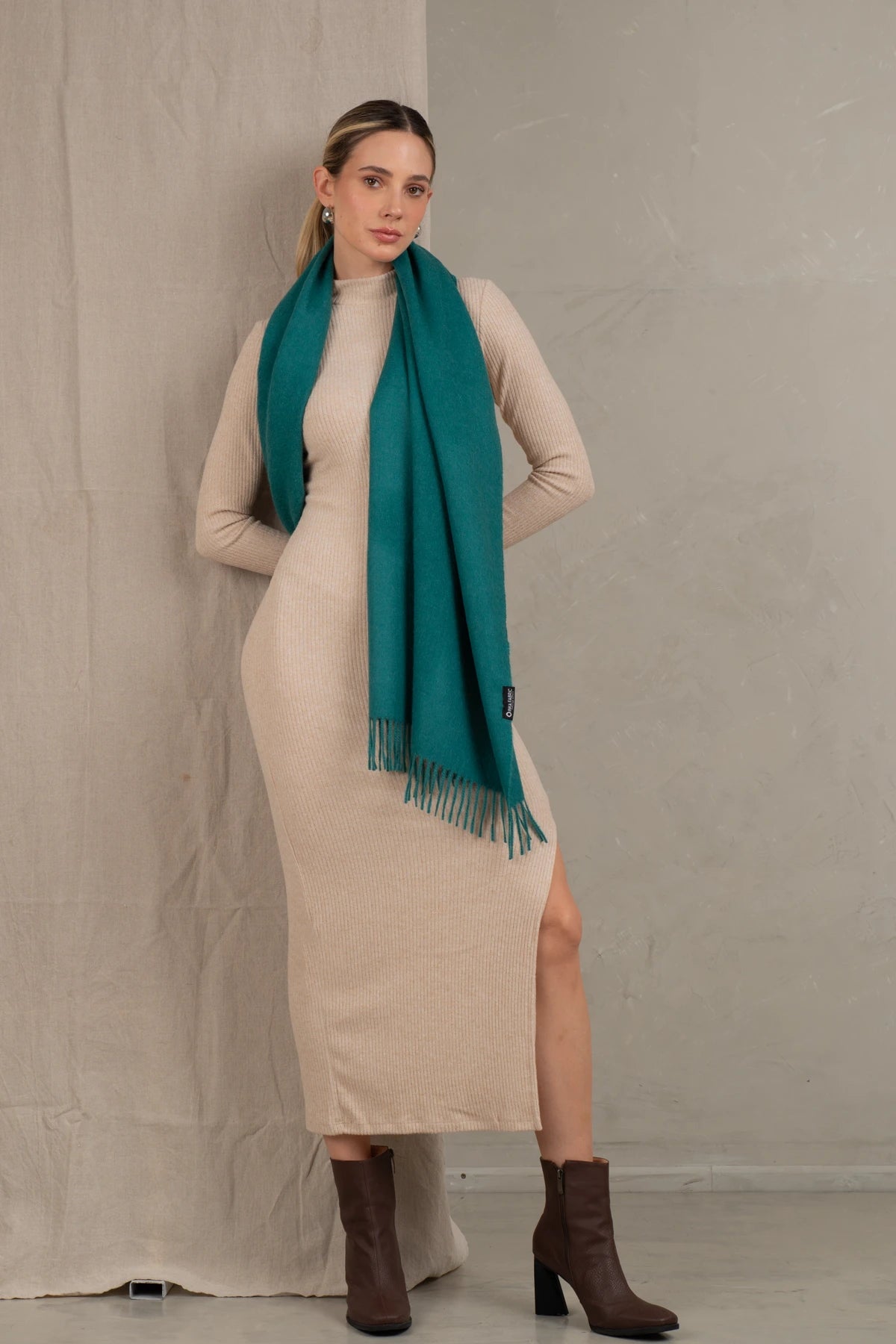 Woman wearing a beige dress and teal scarf against a plain background