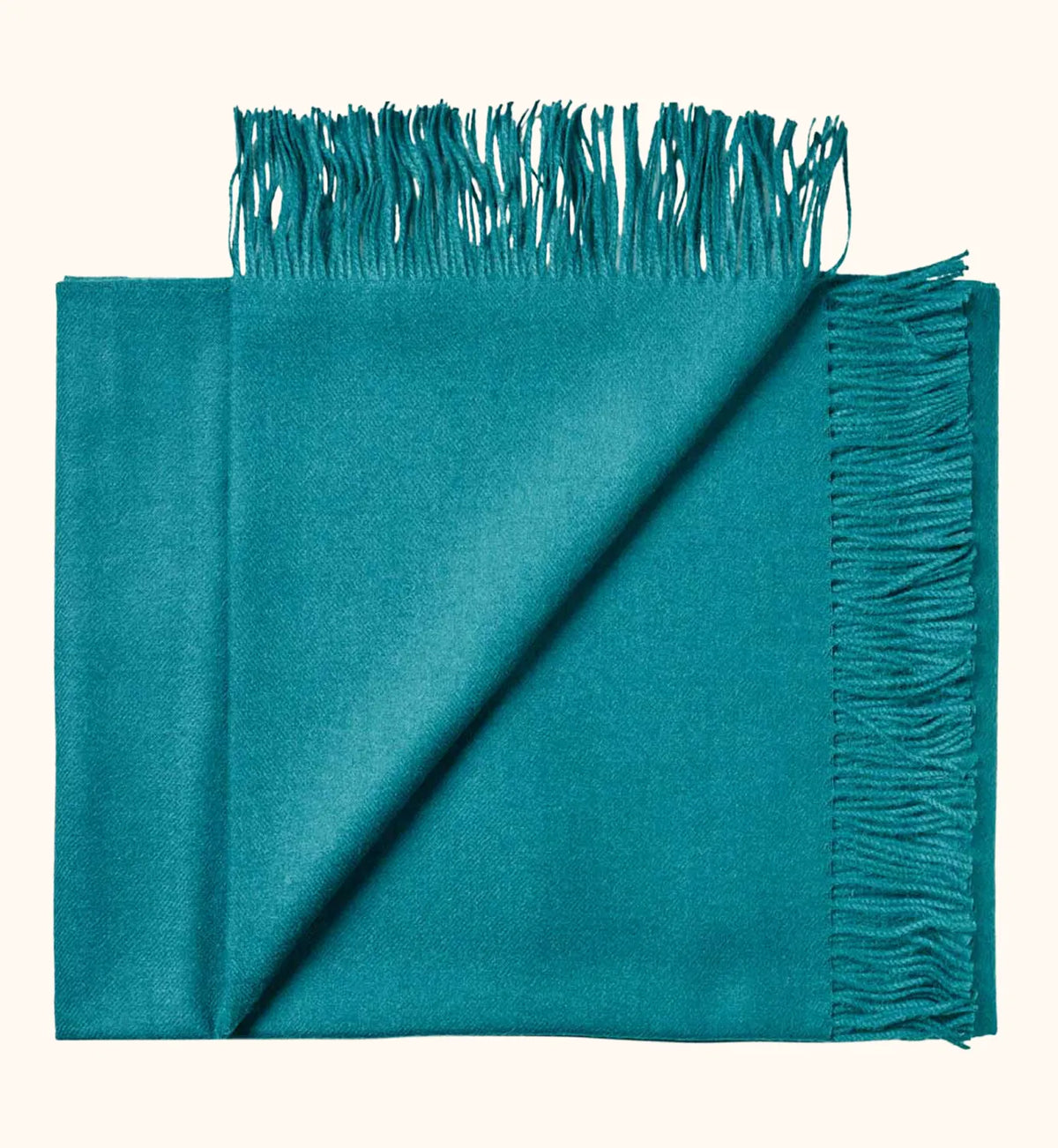 A folded teal blue-green scarf with fringed edges, displayed on a light cream background.