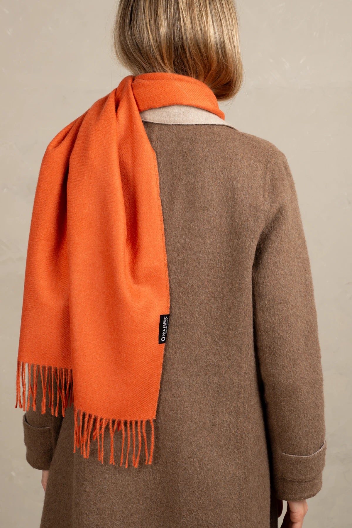 Person wearing an orange alpaca scarf and brown coat against a beige background