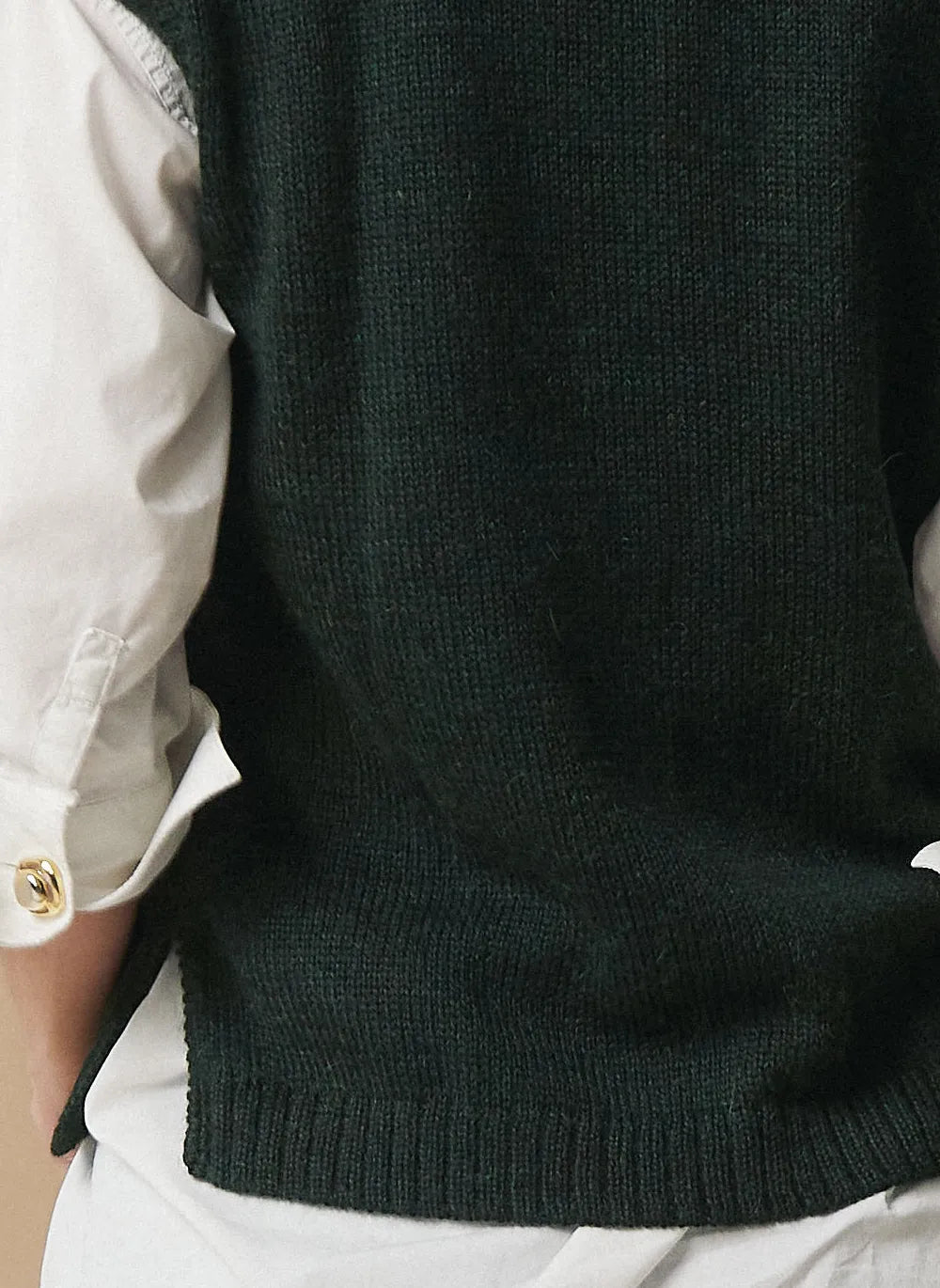 Close-up of a person wearing a dark forest green ribbed knit sweater vest over a white button-up shirt.