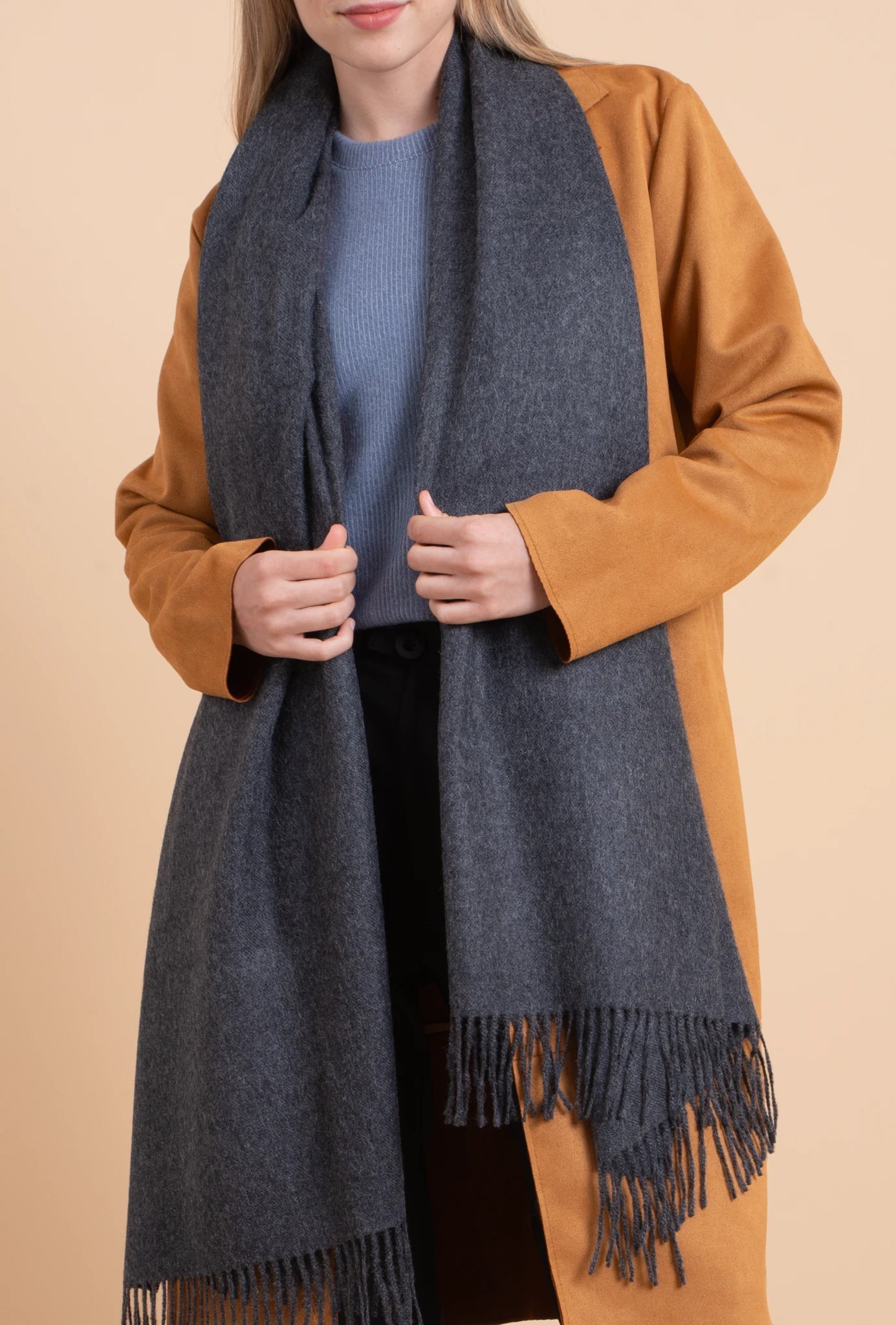 Person wearing a blue scarf and brown coat on a beige background