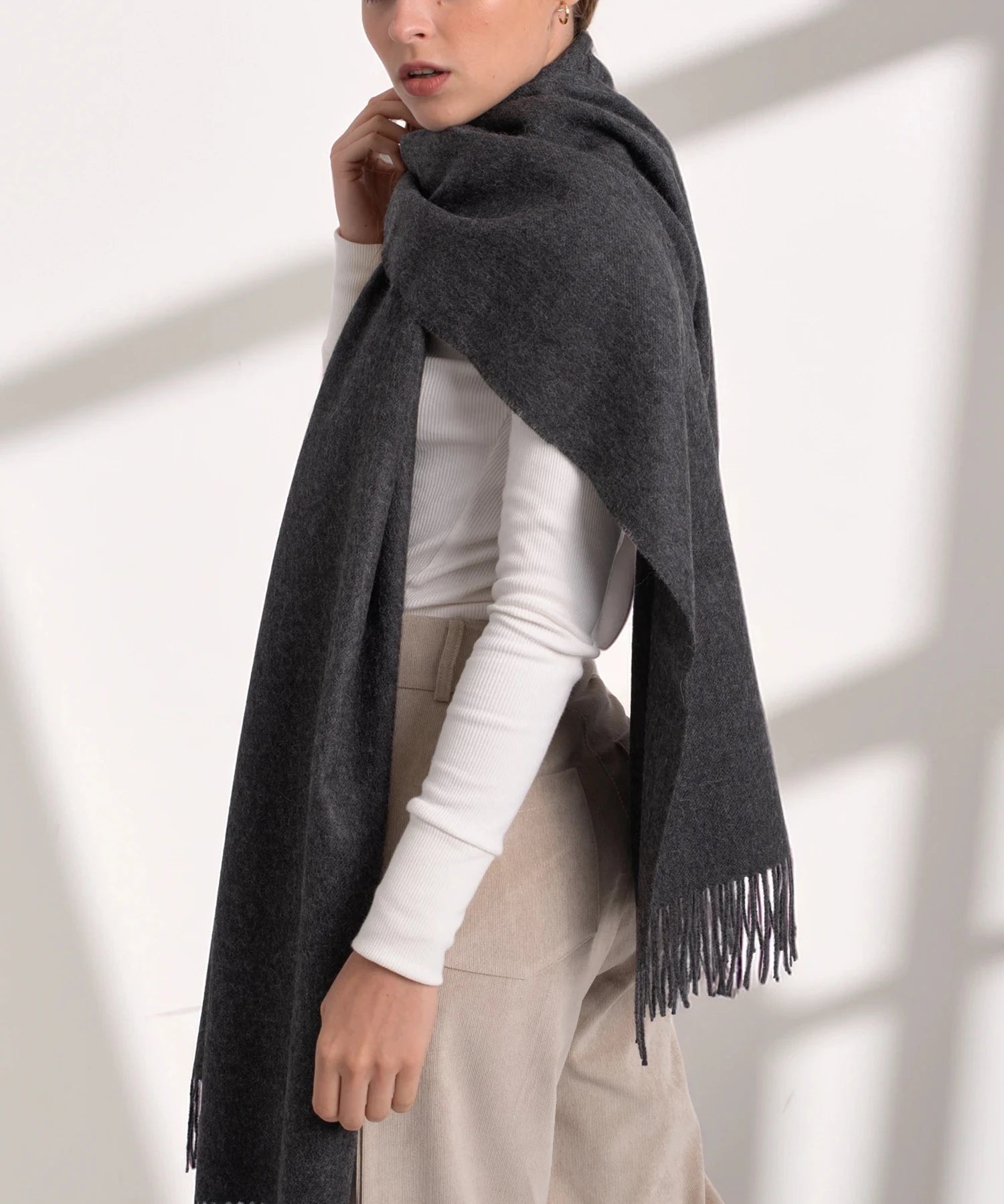 Person wearing a dark gray scarf with a white shirt and beige pants on a light background