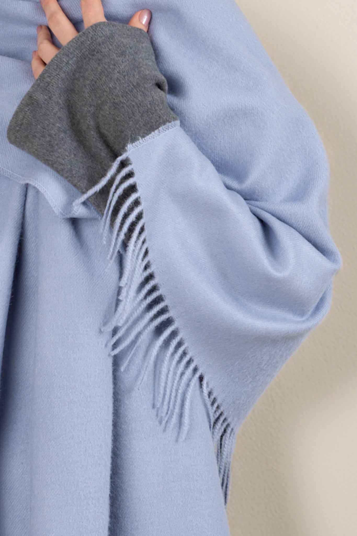 Light blue blanket with gray arm cover and fringe details on a beige background