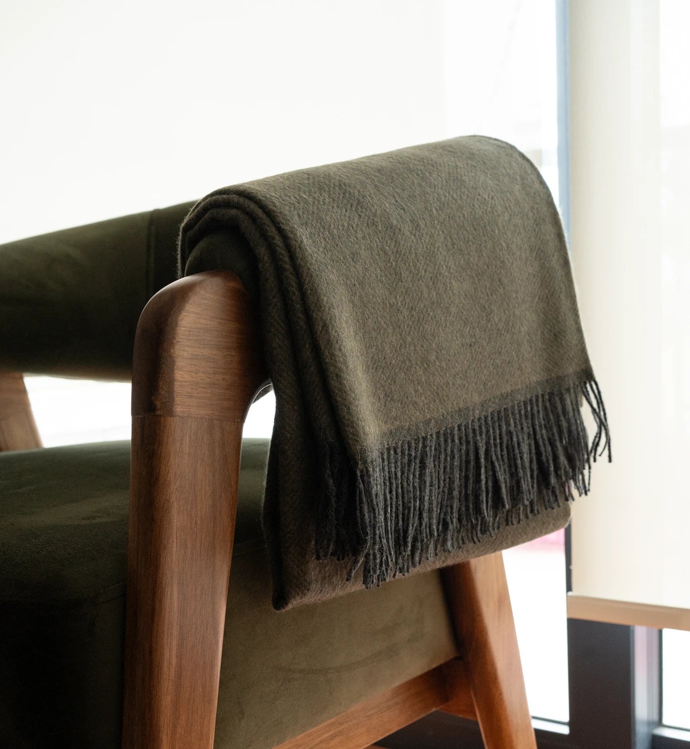 Green blanket draped over a wooden chair with a blurred background