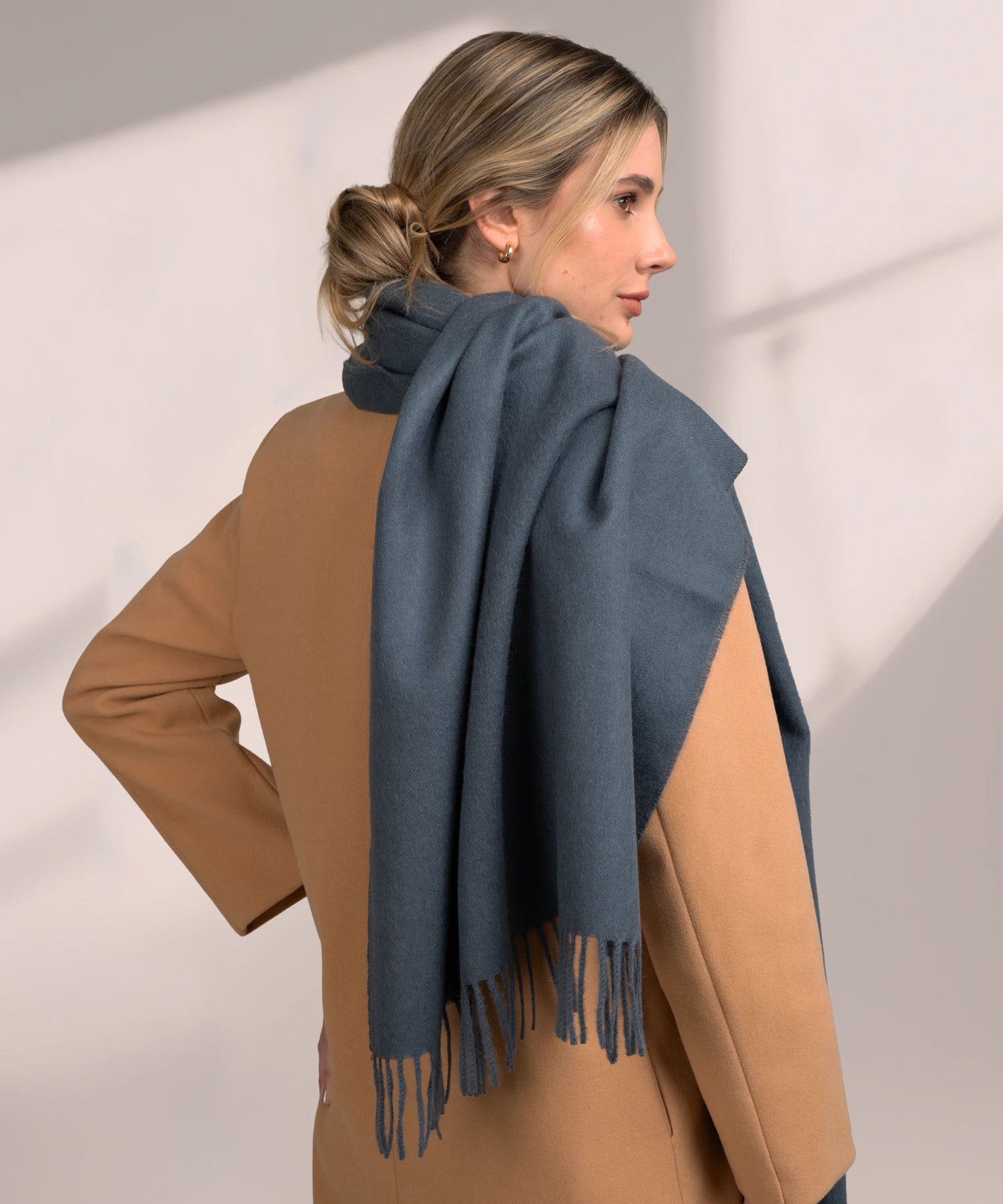 Woman wearing a blue scarf and brown coat against a plain background