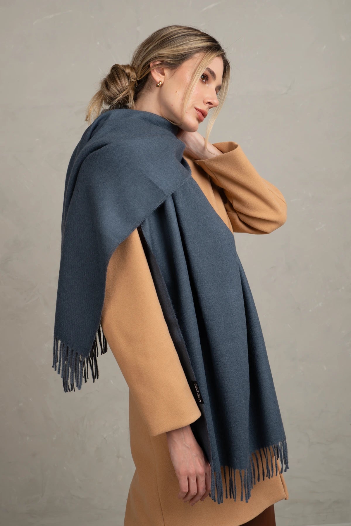 Woman wearing a alpaca  blue scarf with fringe on a plain background