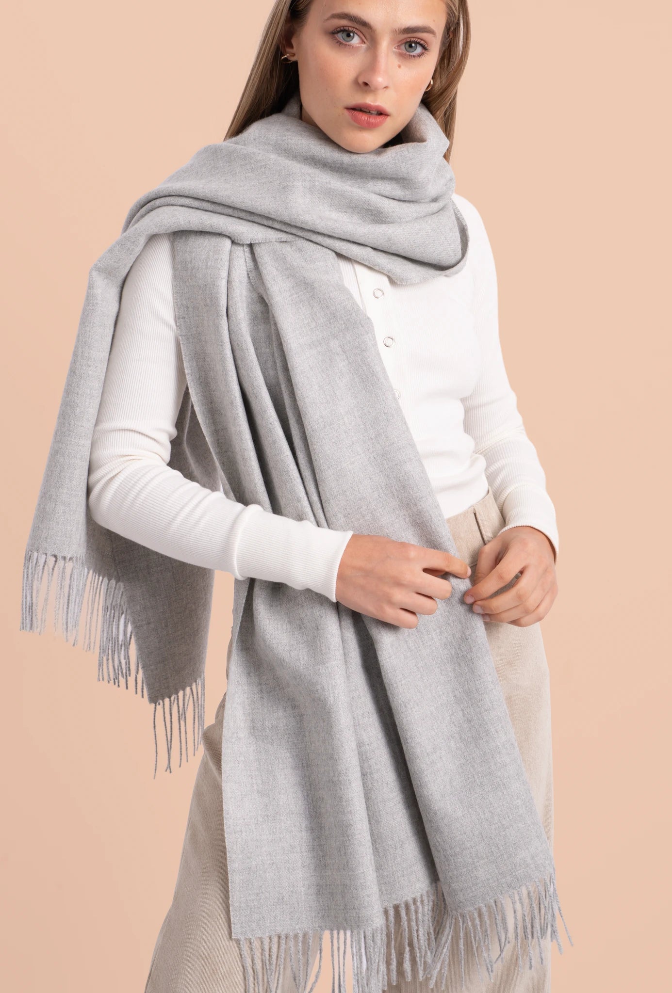 Woman wearing a gray scarf with fringe on a beige background