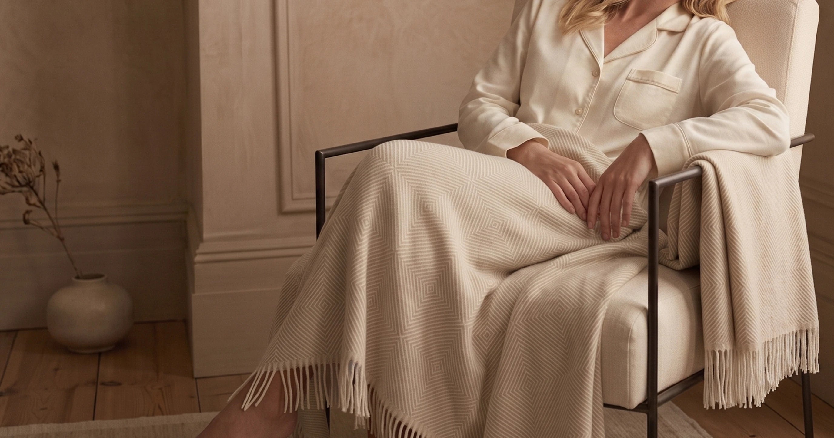 Woman sitting in a chair with a beige blanket draped over her lap in a cozy room.