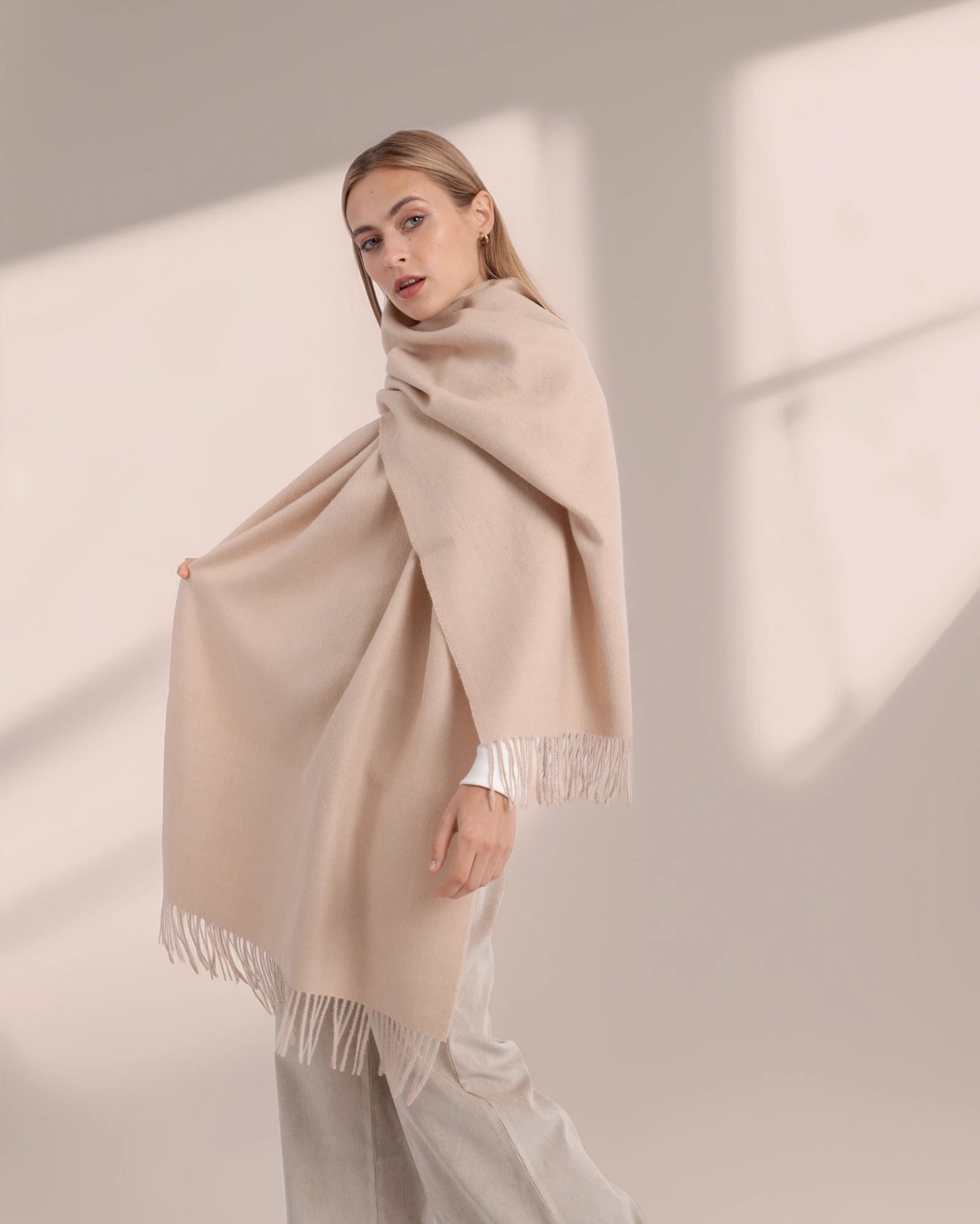 Woman wearing a beige scarf with fringe details on a neutral background