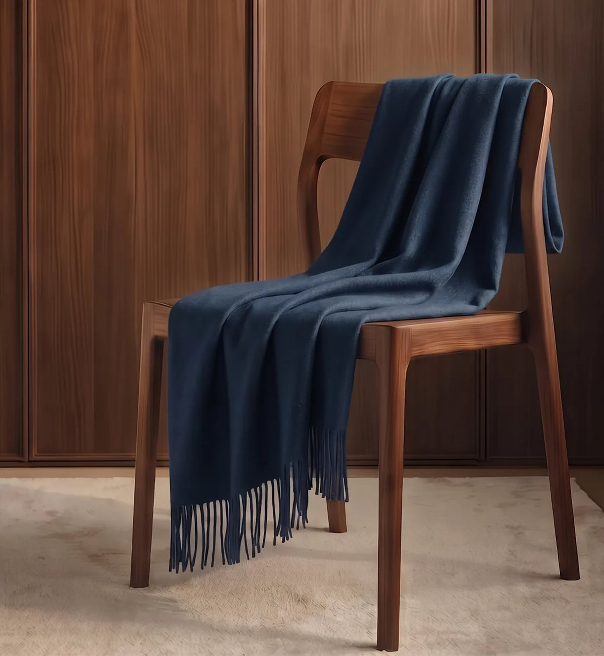 A navy blue knit throw blanket with fringe is draped over a wooden chair in front of a dark wood-paneled wall.