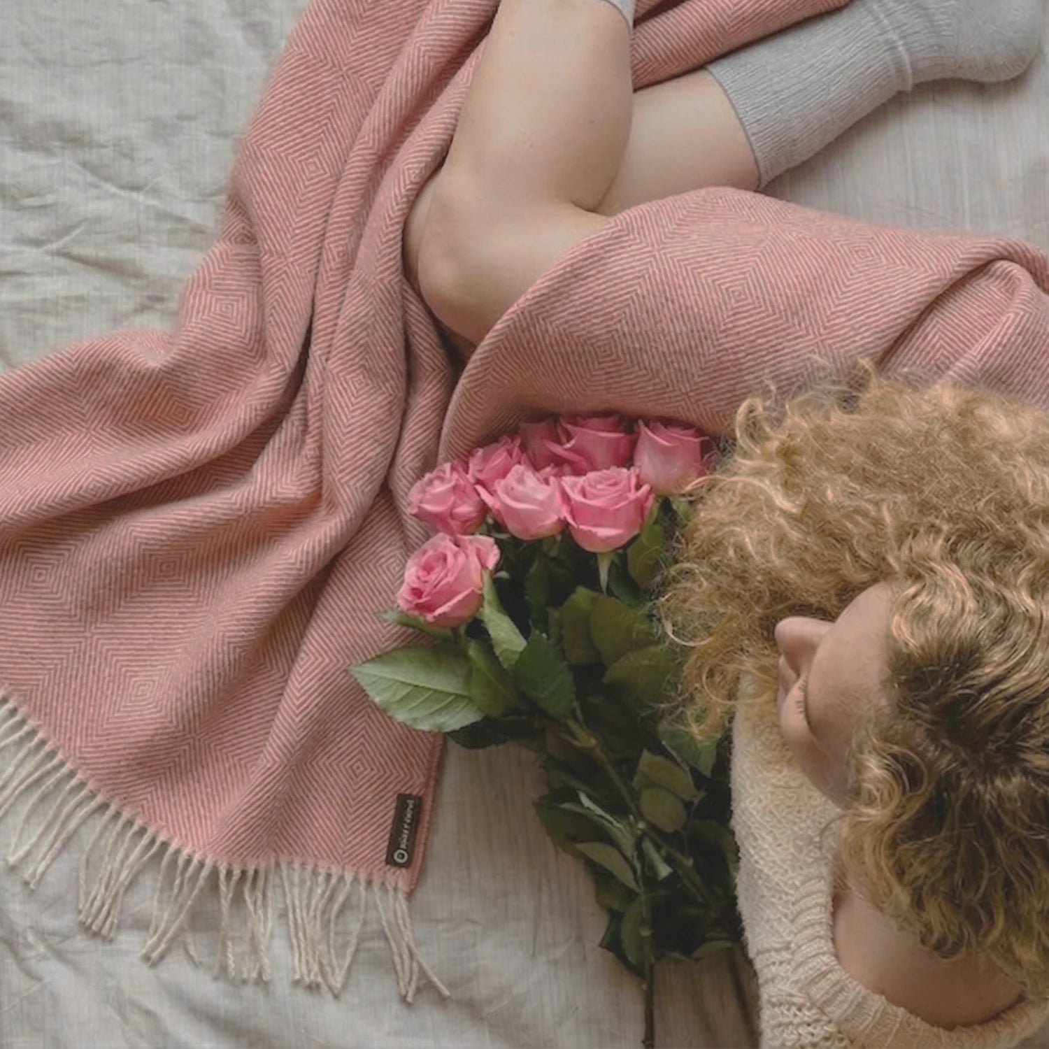 Person lying on a bed with pink roses and a pink blanket