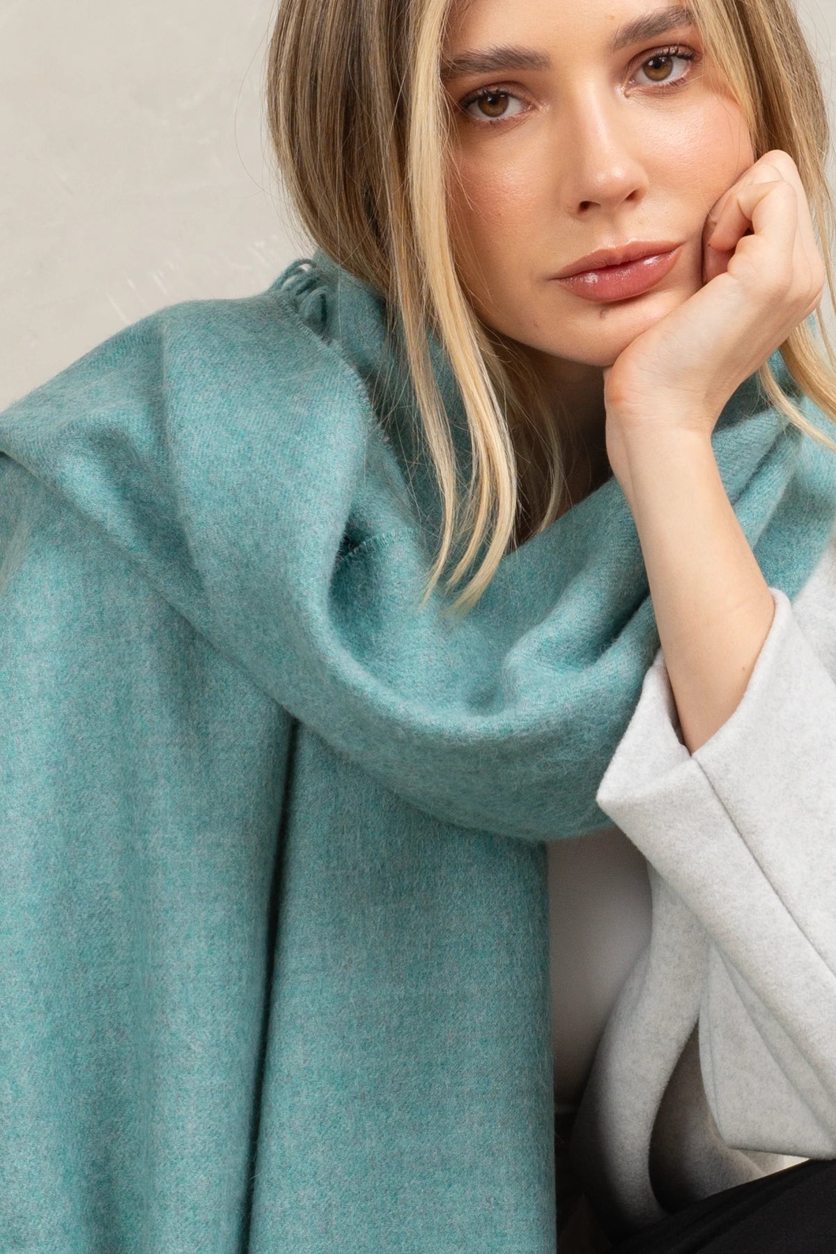 Woman wearing a alpaca  teal scarf with a neutral background