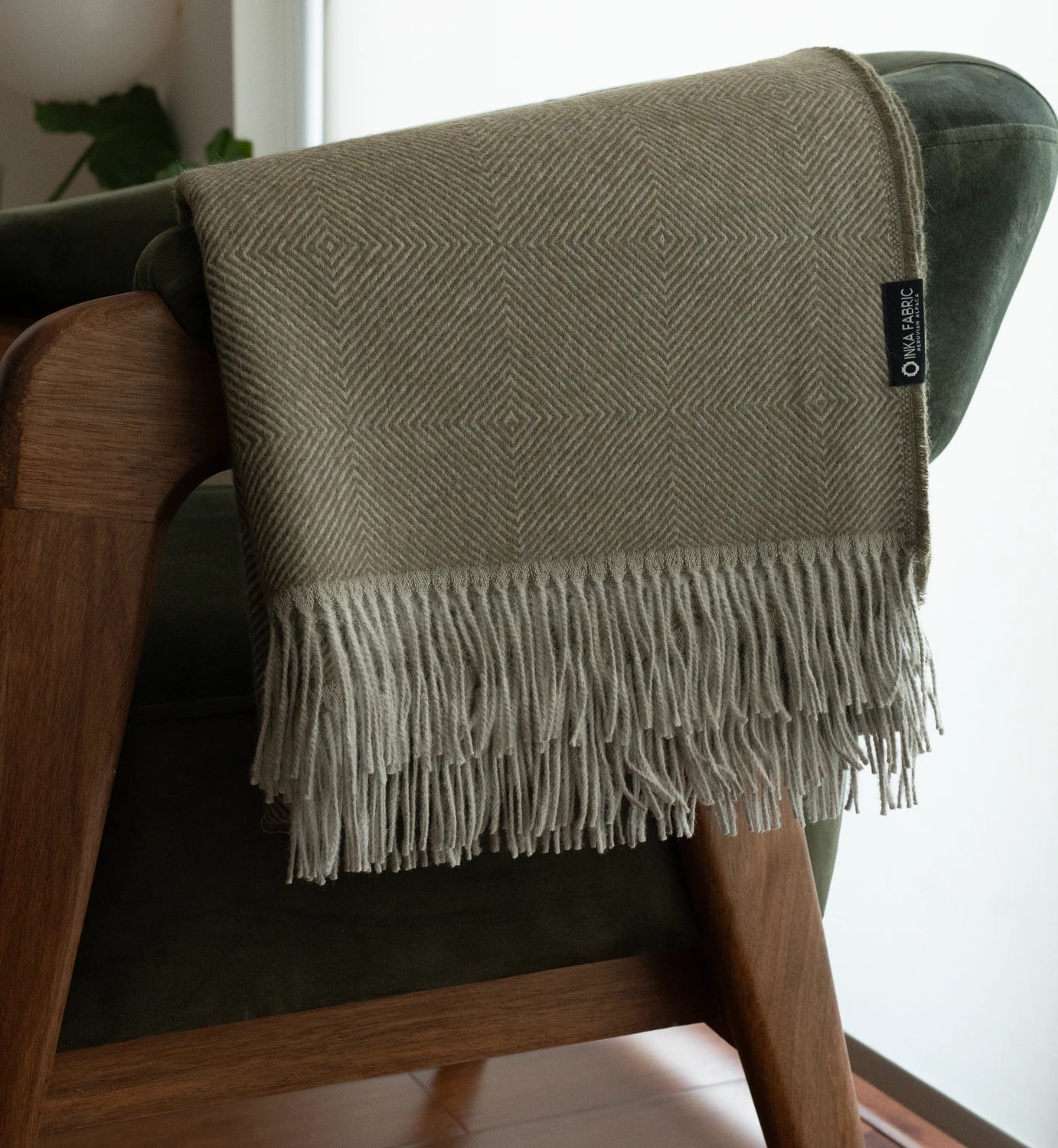 Green woven blanket with fringe draped over a wooden chair.