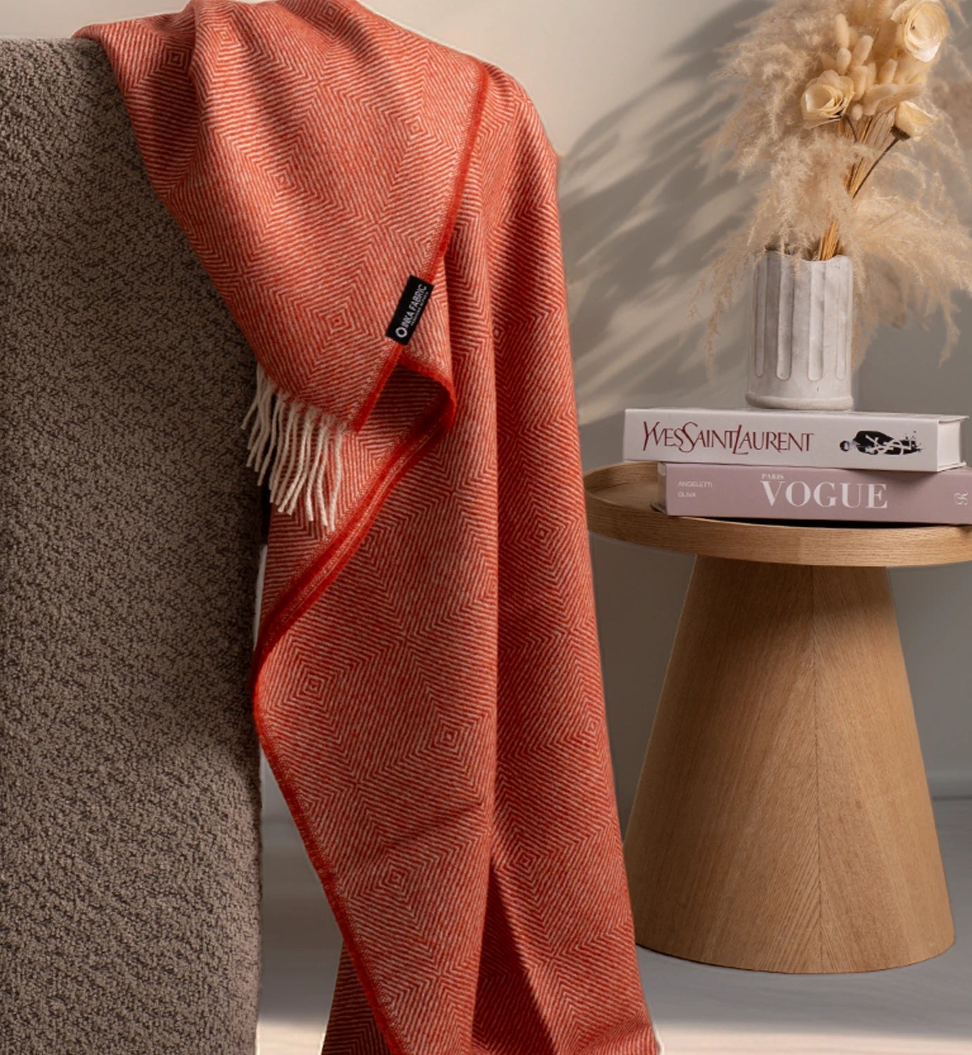 Orange throw blanket draped over a chair next to a wooden side table with books and a vase.