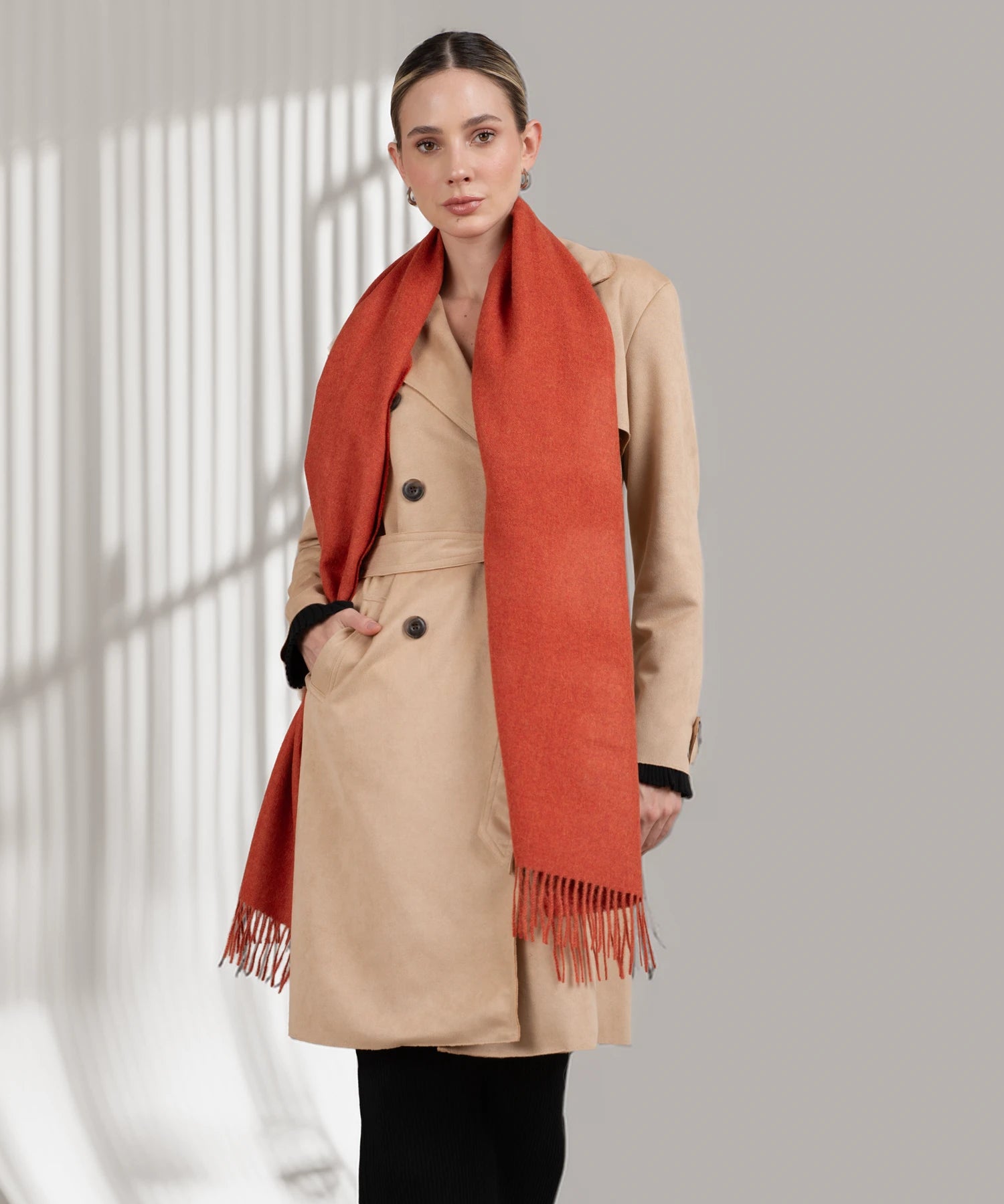 Woman wearing a beige coat and red scarf against a neutral background