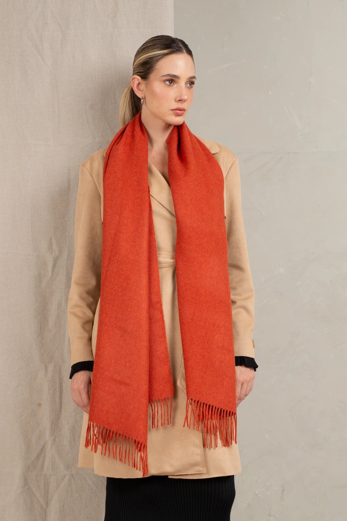Woman wearing a long alpaca wool orange scarf against a neutral background