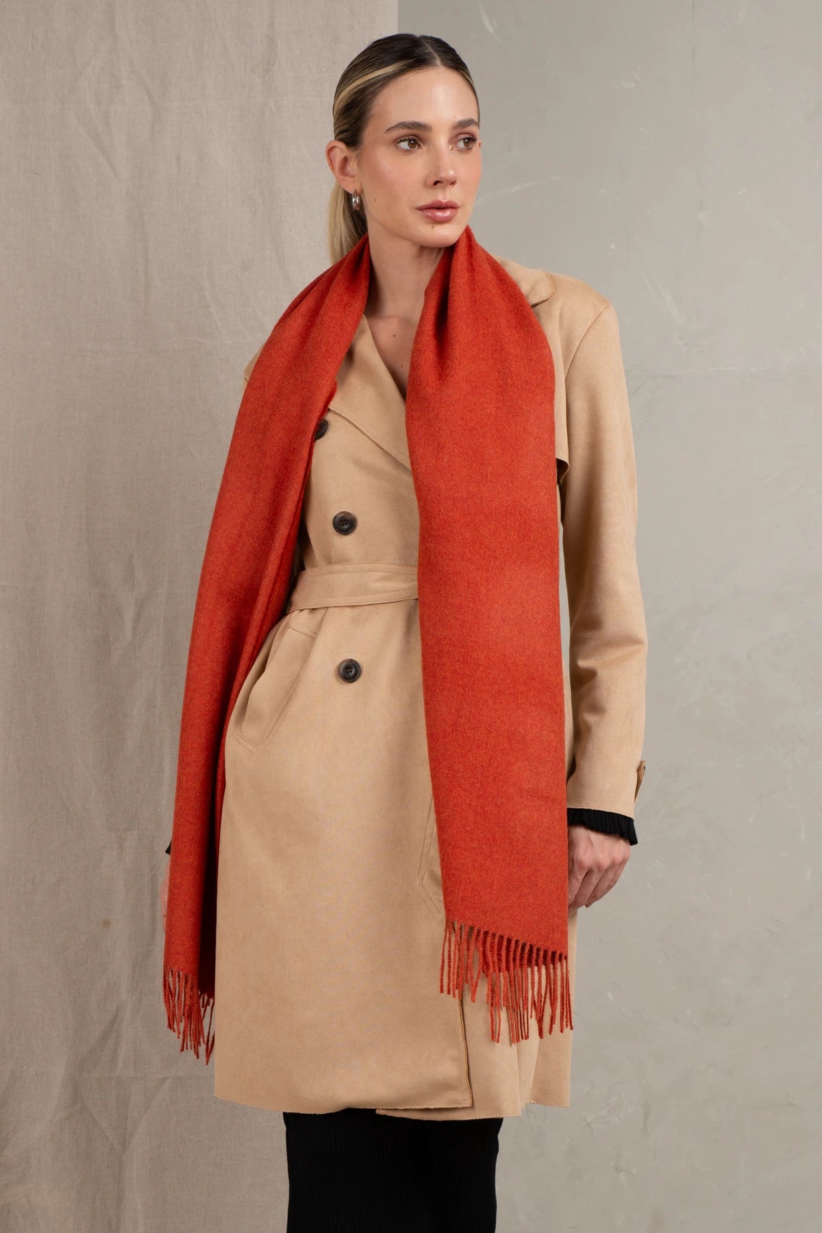 Woman wearing a beige coat and red scarf against a neutral background