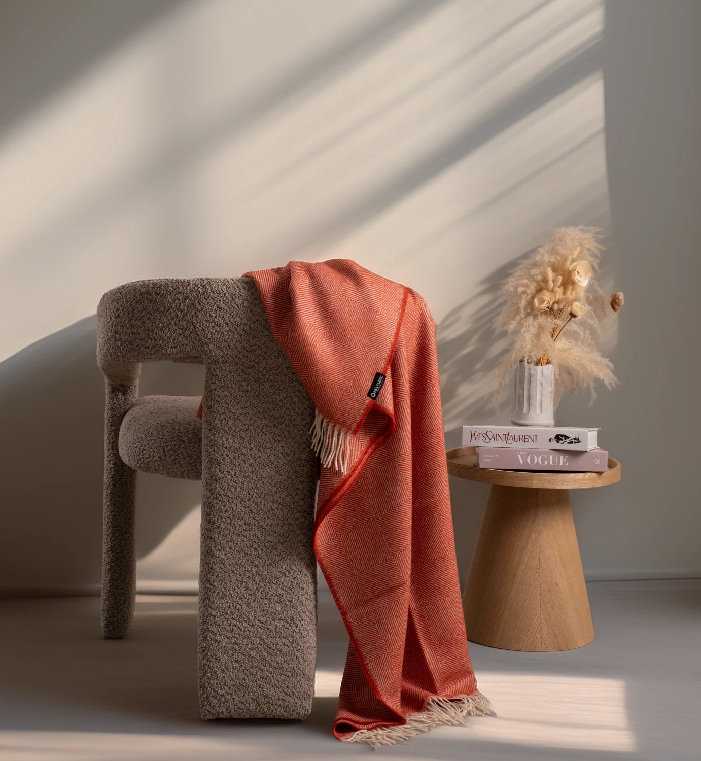 Cushion with a red throw blanket draped over it, placed on a textured surface with a neutral background.